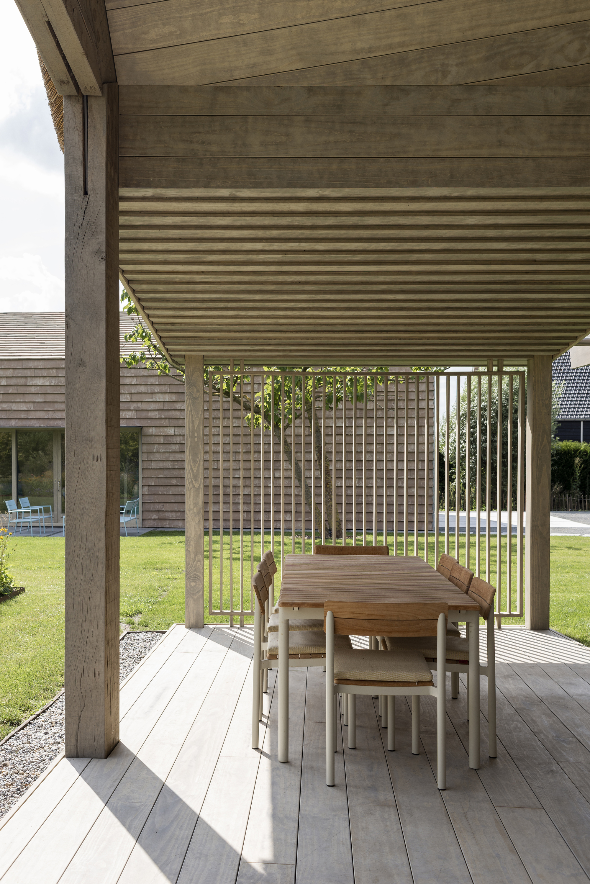 Covered terrace with timber decking and vertical slat railing overlooking a lawn