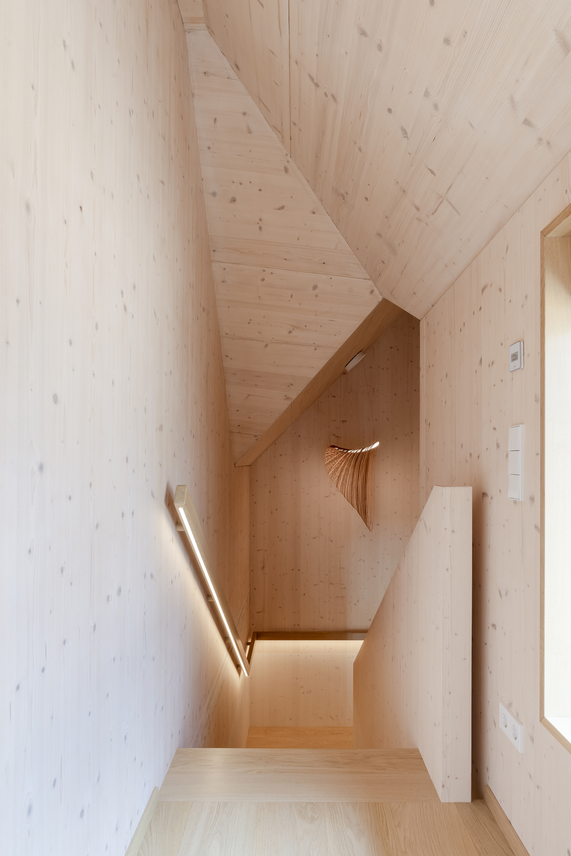 Light-wood-paneled stairwell with a sculptural pendant lamp and daylight from a skylight above