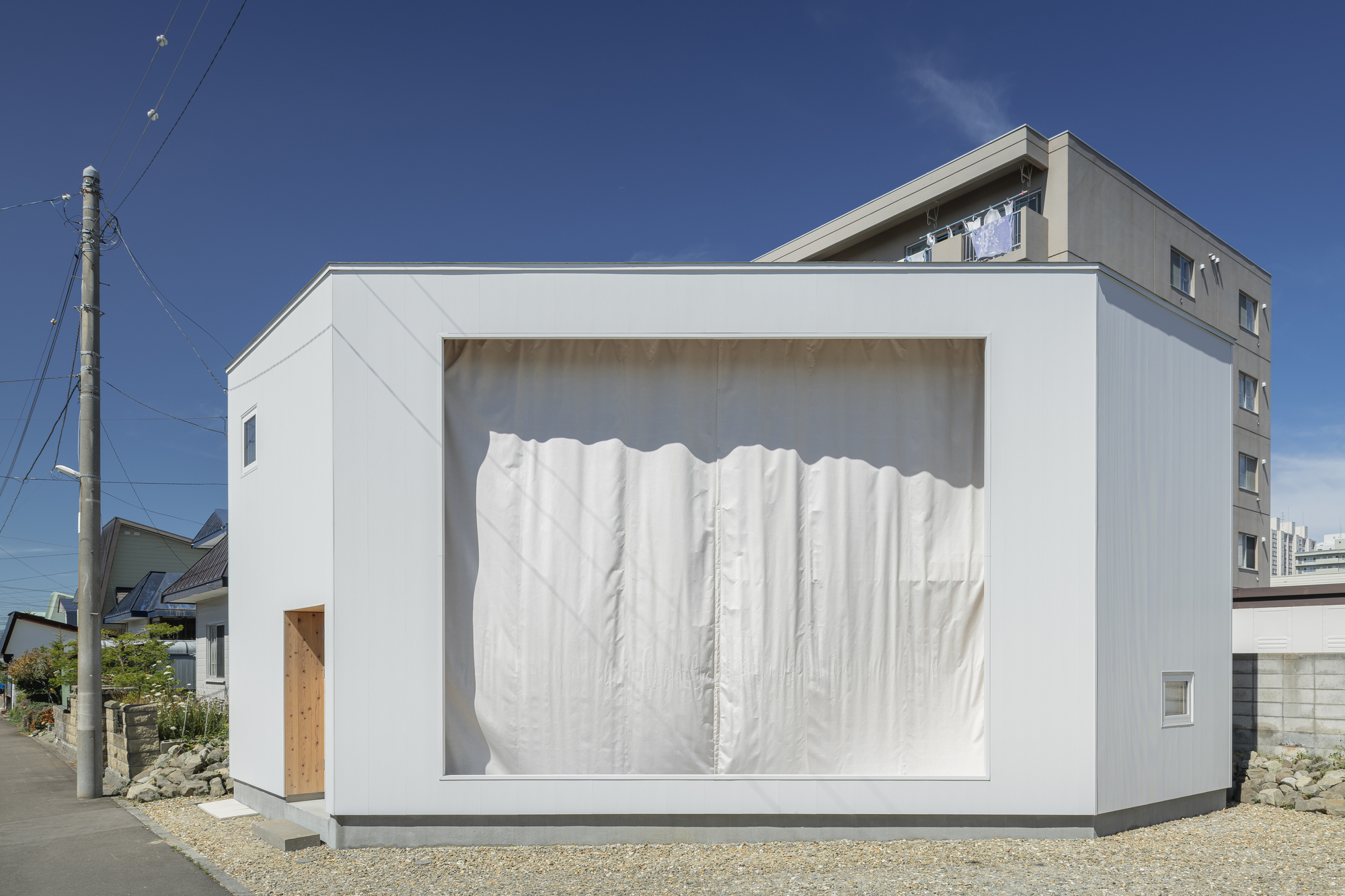 White facade frame with plywood reveals and closed white fabric curtains screening the interior