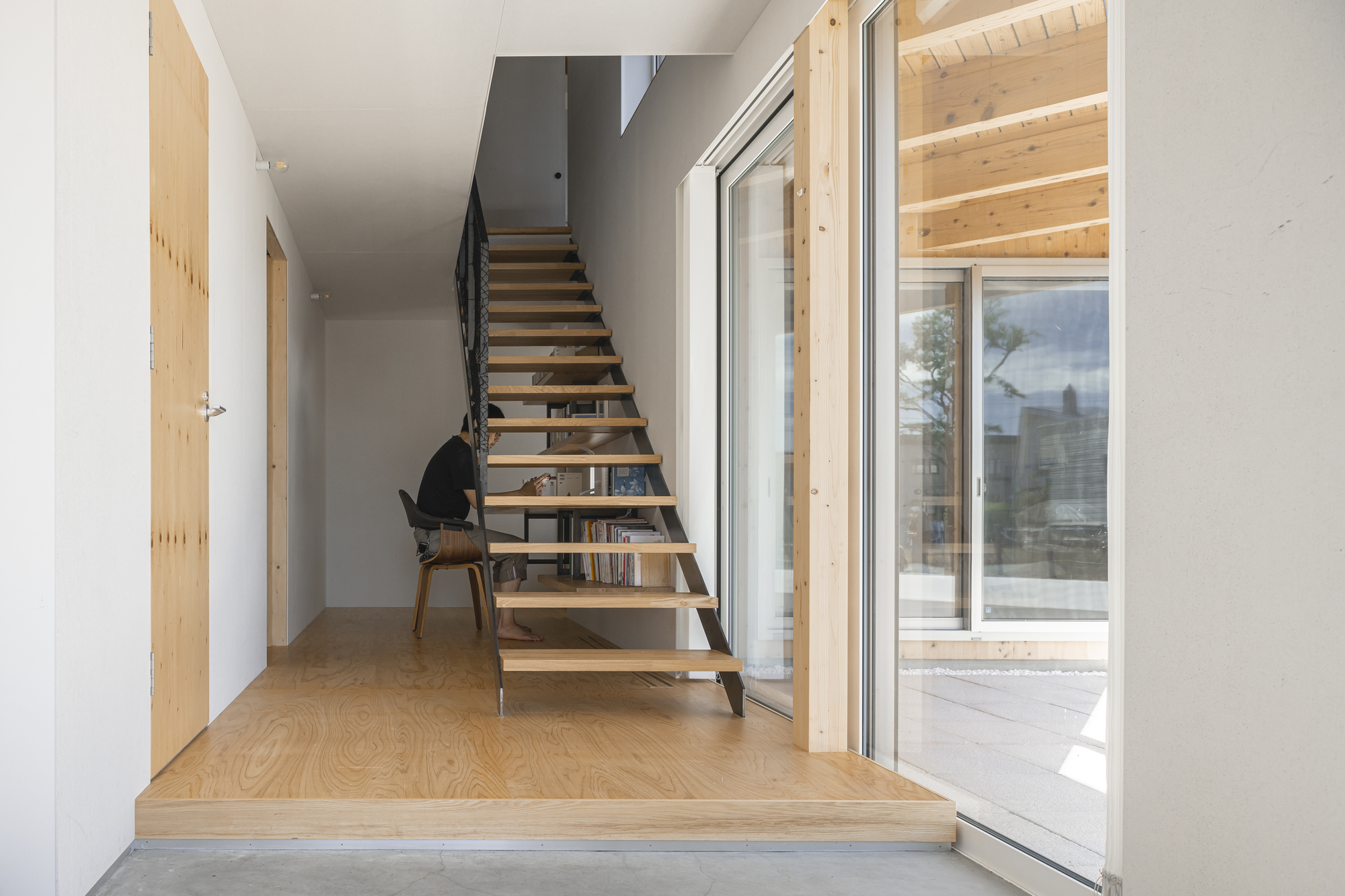 Entry hallway with open timber staircase and plywood flooring leading to glazed doors