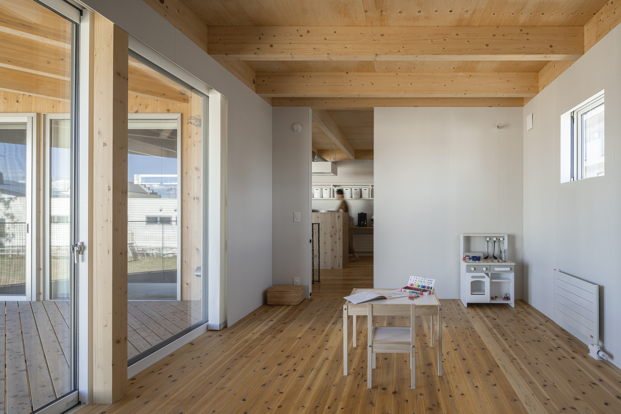 Open living space with exposed timber ceiling beams and a figure moving through the kitchen