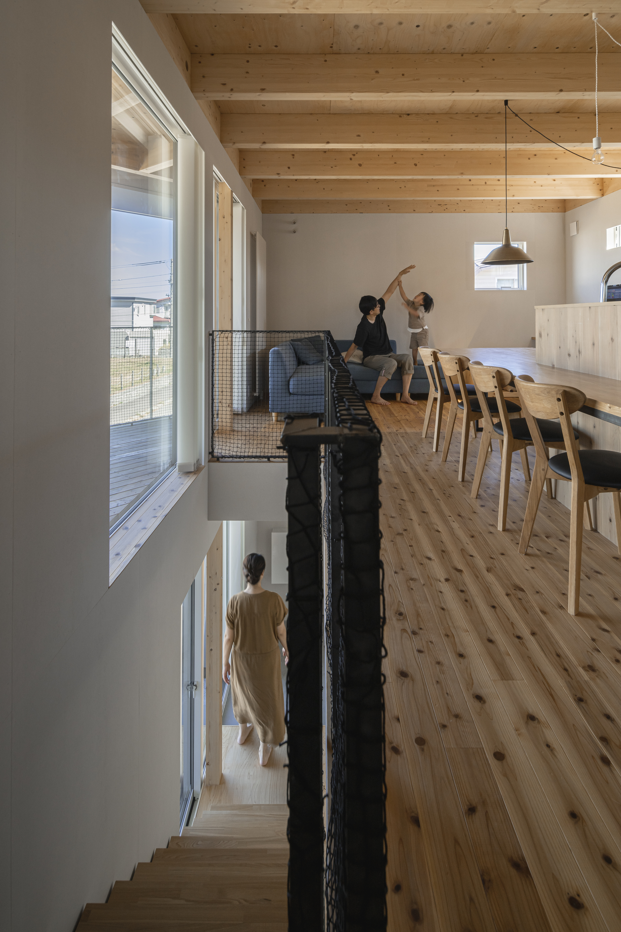 Split-level interior with exposed timber ceiling beams, mesh-rail balustrade, and residents moving through the upper floor