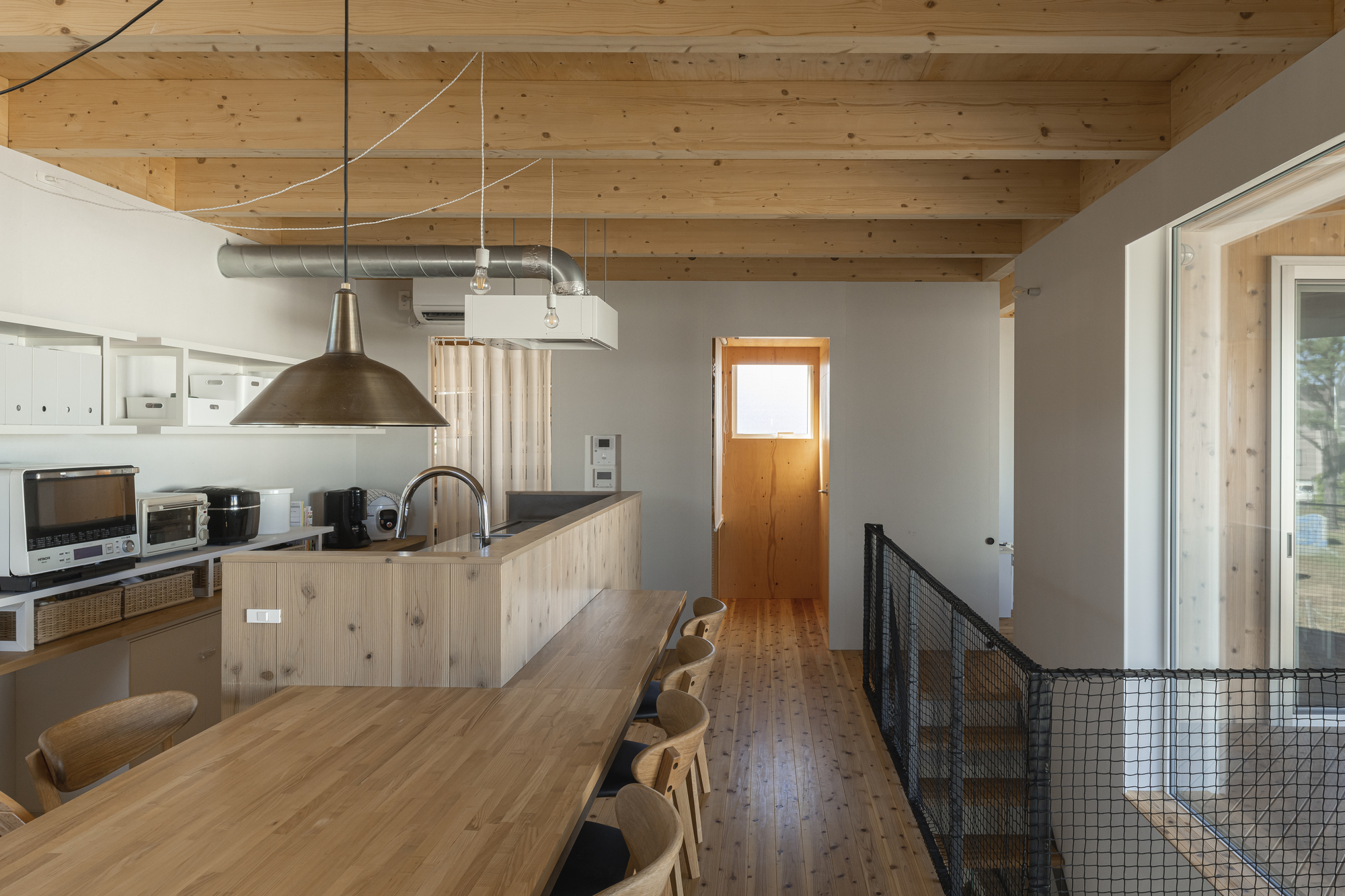 Open kitchen with timber island bench, exposed ductwork, and wire mesh guardrail at stair opening