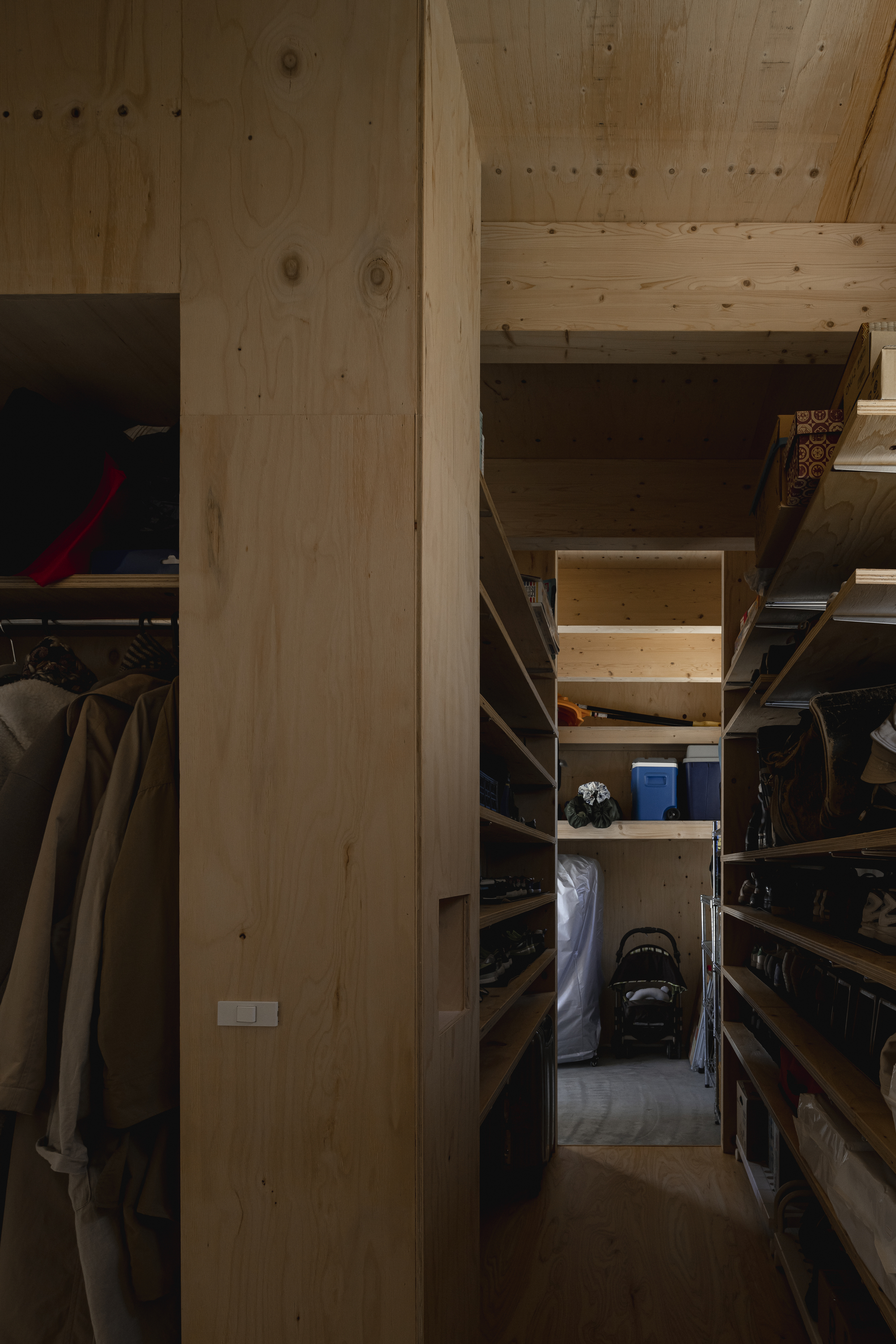 Narrow storage corridor lined with timber shelving under a plywood ceiling in low light