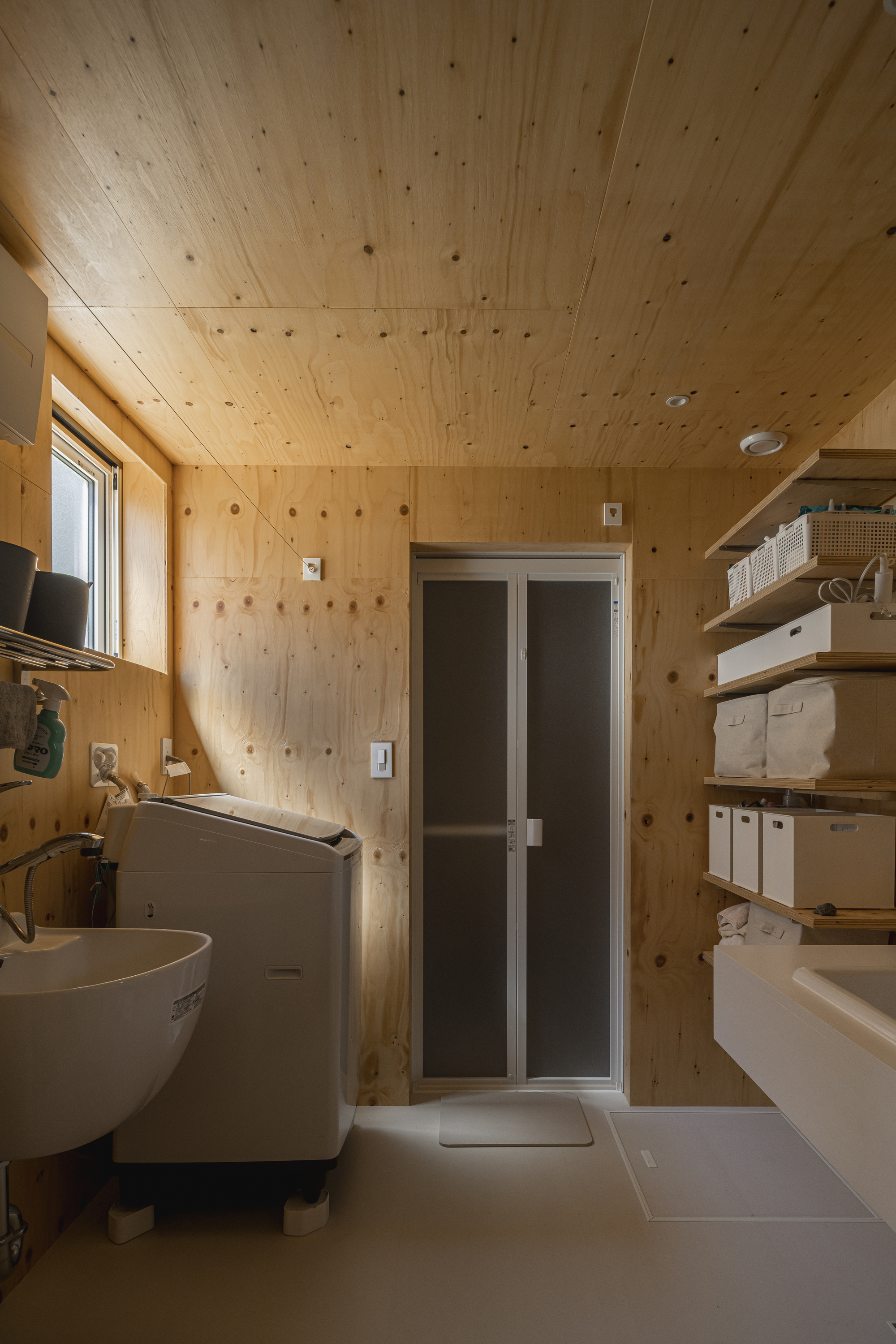Compact bathroom clad entirely in plywood with wall-mounted sink and frosted glass shower door