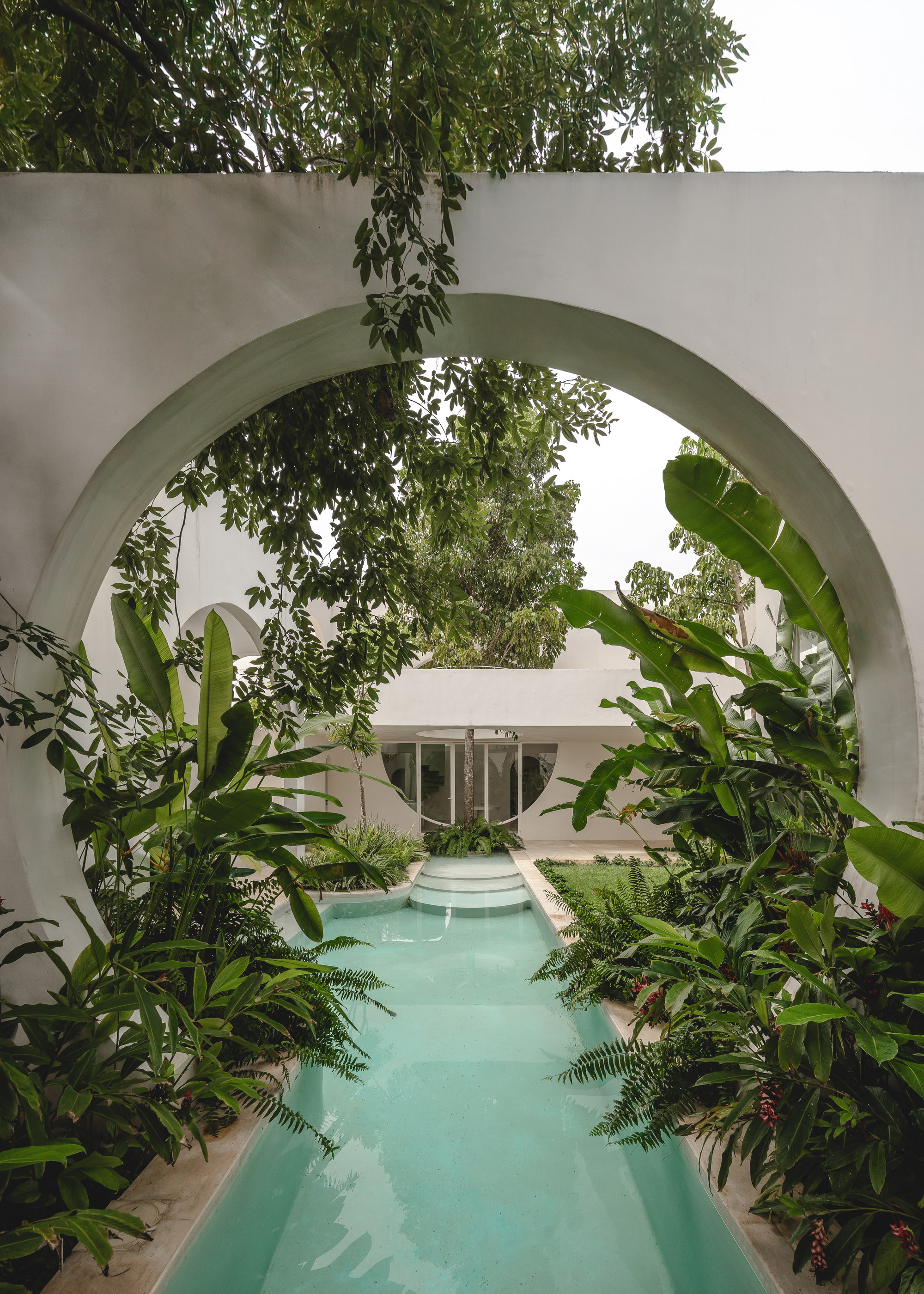 Courtyard pool with turquoise water viewed through two stacked arches surrounded by ferns, palms, and banana plants