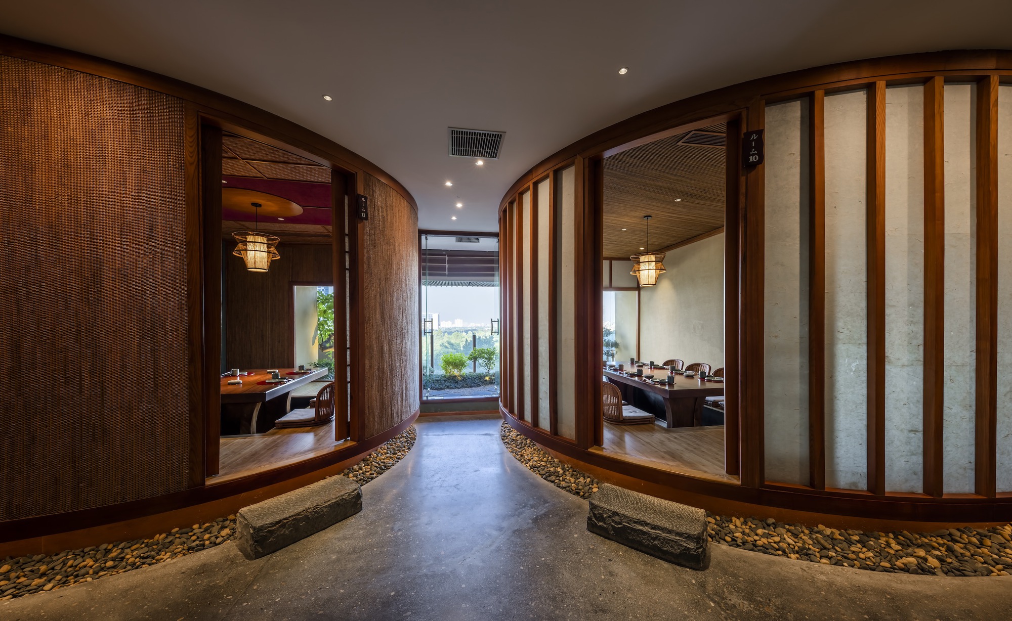 Corridor with curved timber screen walls and river stone flooring flanked by translucent shoji-style partitions