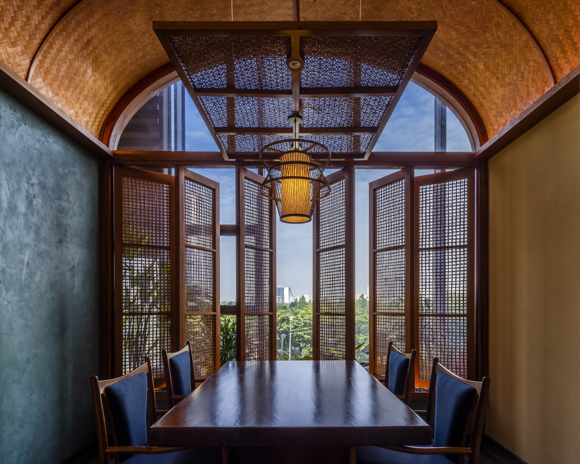 Private dining alcove with woven rattan screens framing a view to greenery through arched openings
