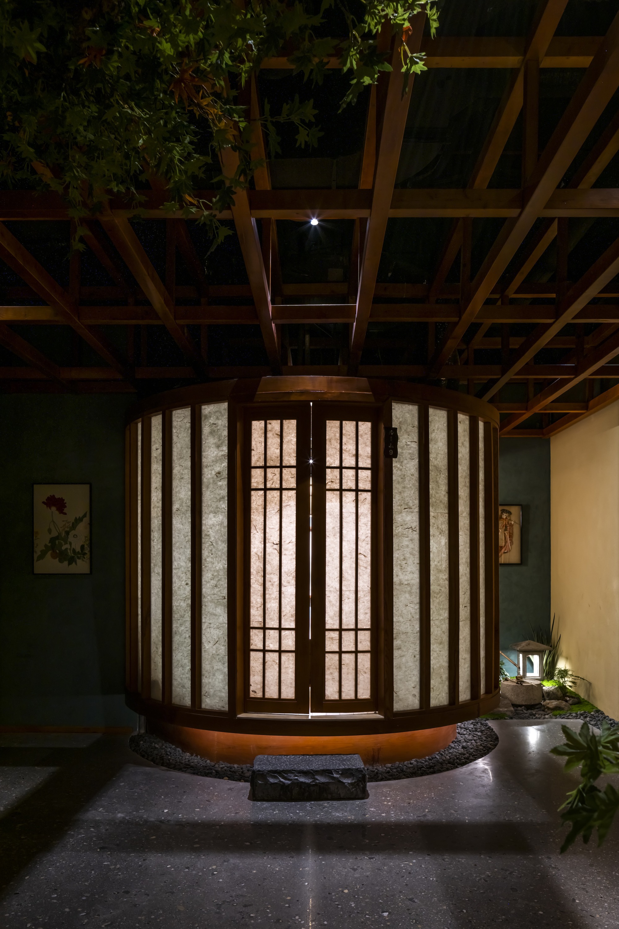 Cylindrical entry pavilion with timber frame and translucent paper panels beneath an exposed wood beam ceiling at night