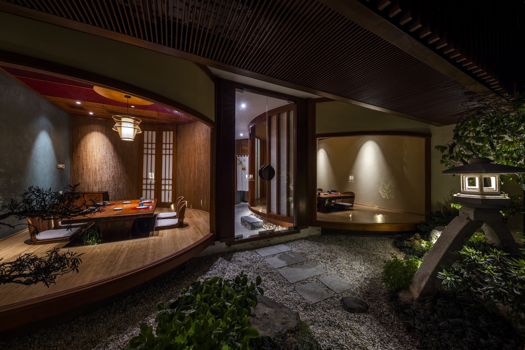 Courtyard view at night showing curved dining room, central corridor, and planted gravel garden with stepping stones