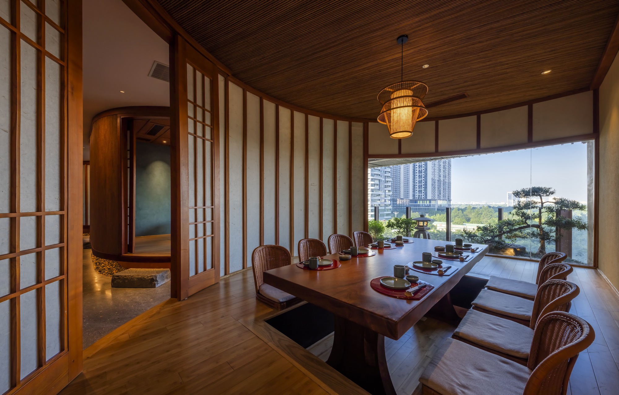 Dining room with low table and sliding shoji screens opening to a terrace with bonsai tree