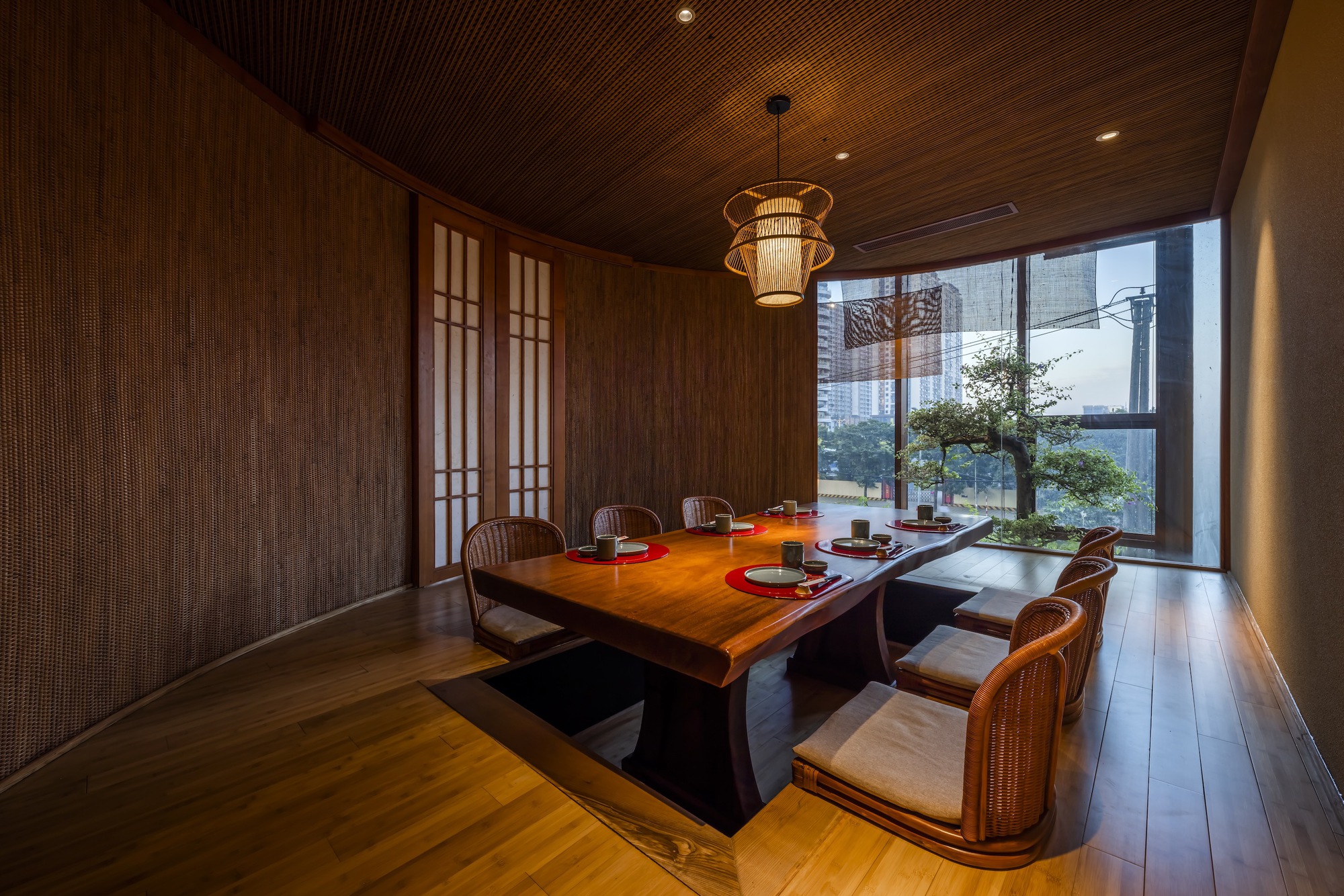 Private dining room with slatted timber ceiling and woven pendant light overlooking a courtyard tree
