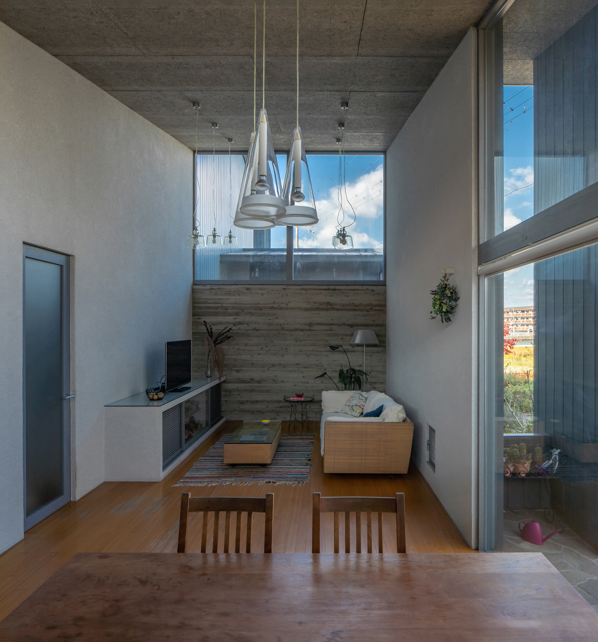 Double-height living space with exposed concrete ceiling, glass pendant lights, and timber accent wall