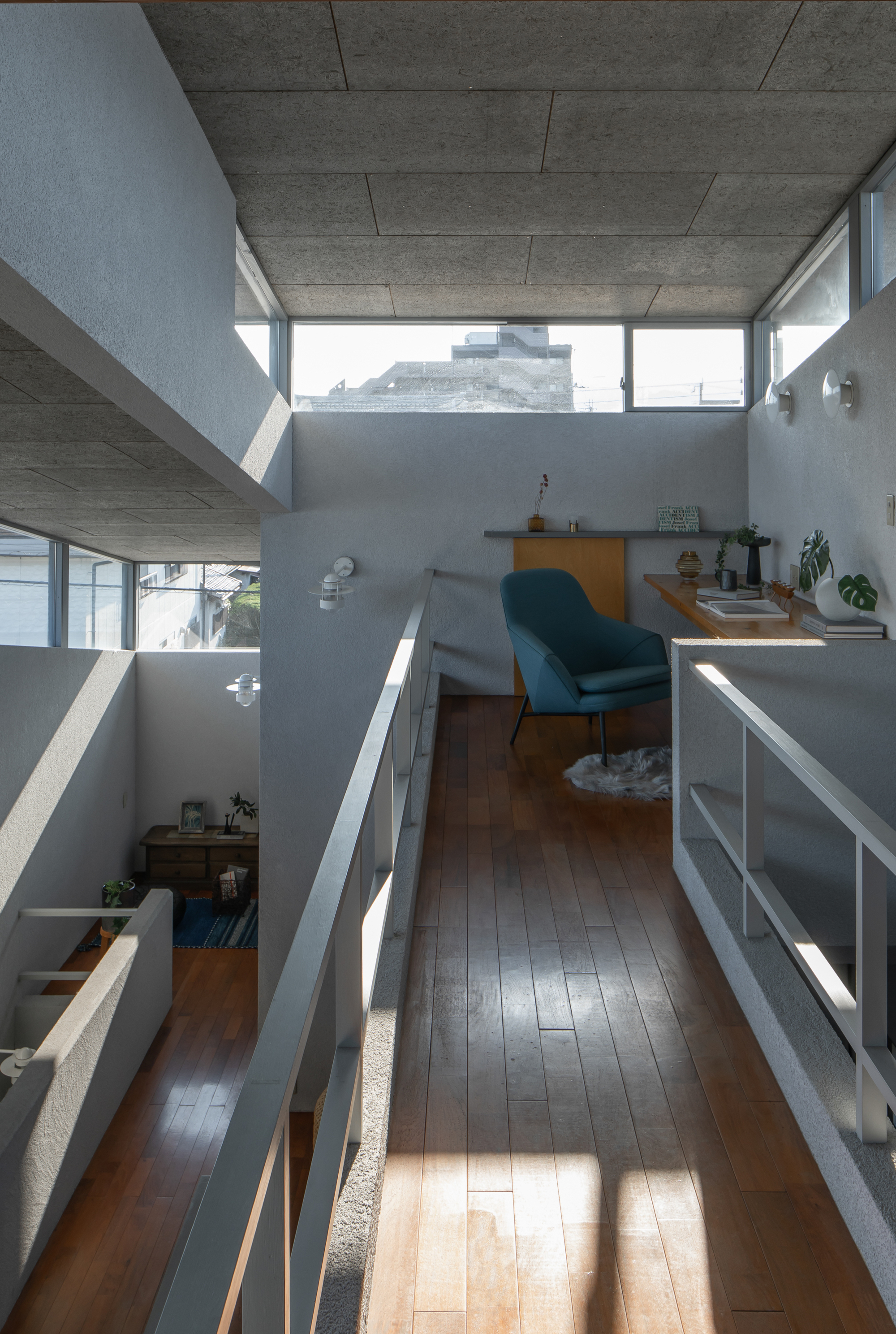 Upper-level hallway overlooking split-level interior spaces with exposed concrete ceiling and angular clerestory windows