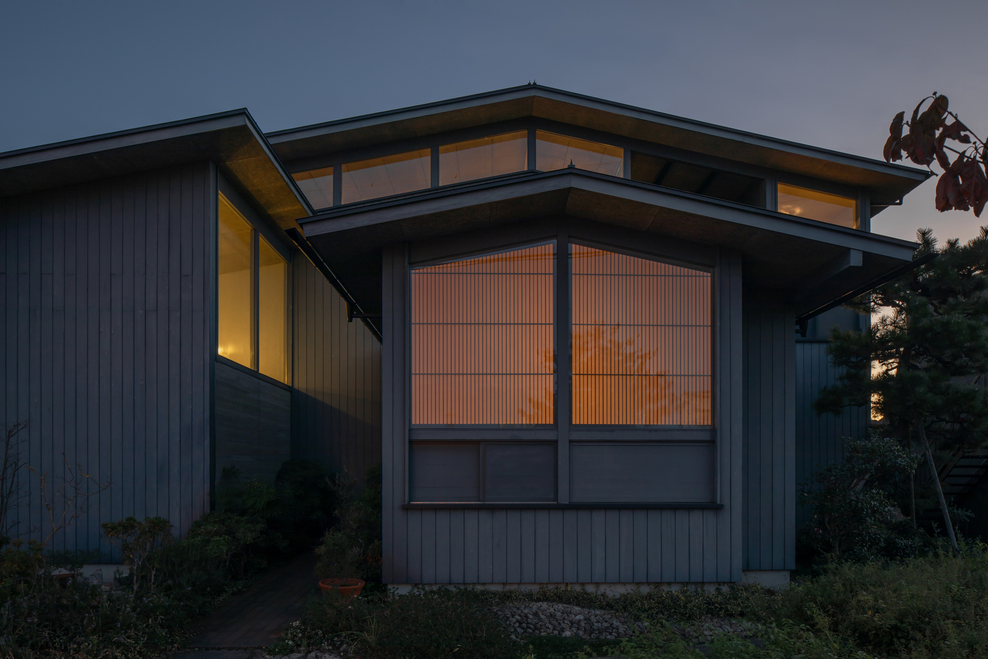 Dark vertical wood siding facade with illuminated window frames glowing at dusk