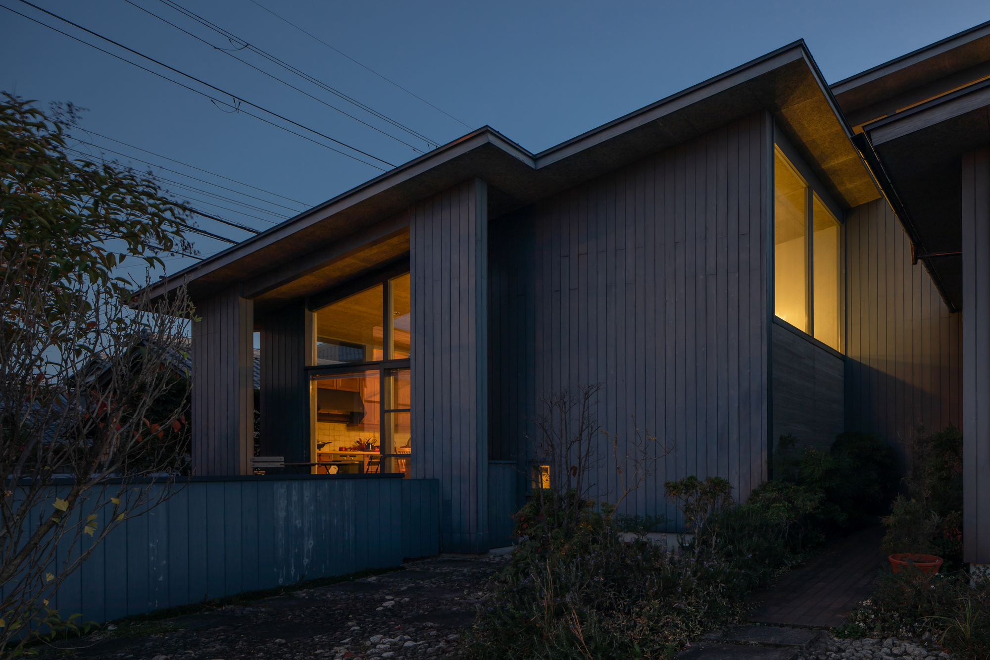 Exterior view showing vertical siding volumes with lit windows and low plantings at twilight