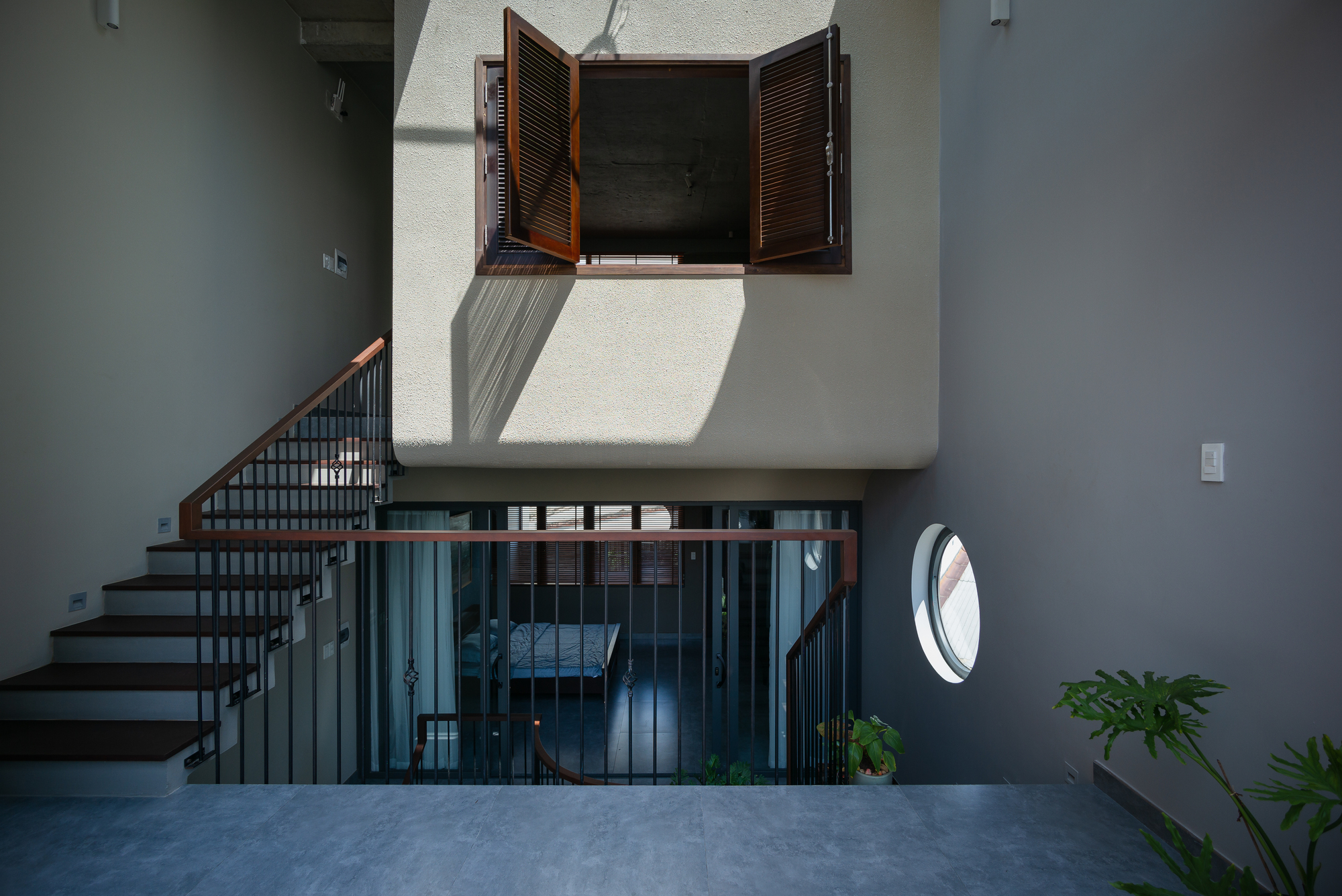 Interior staircase with timber handrail and black metal balustrade connecting multiple levels under open timber shutters