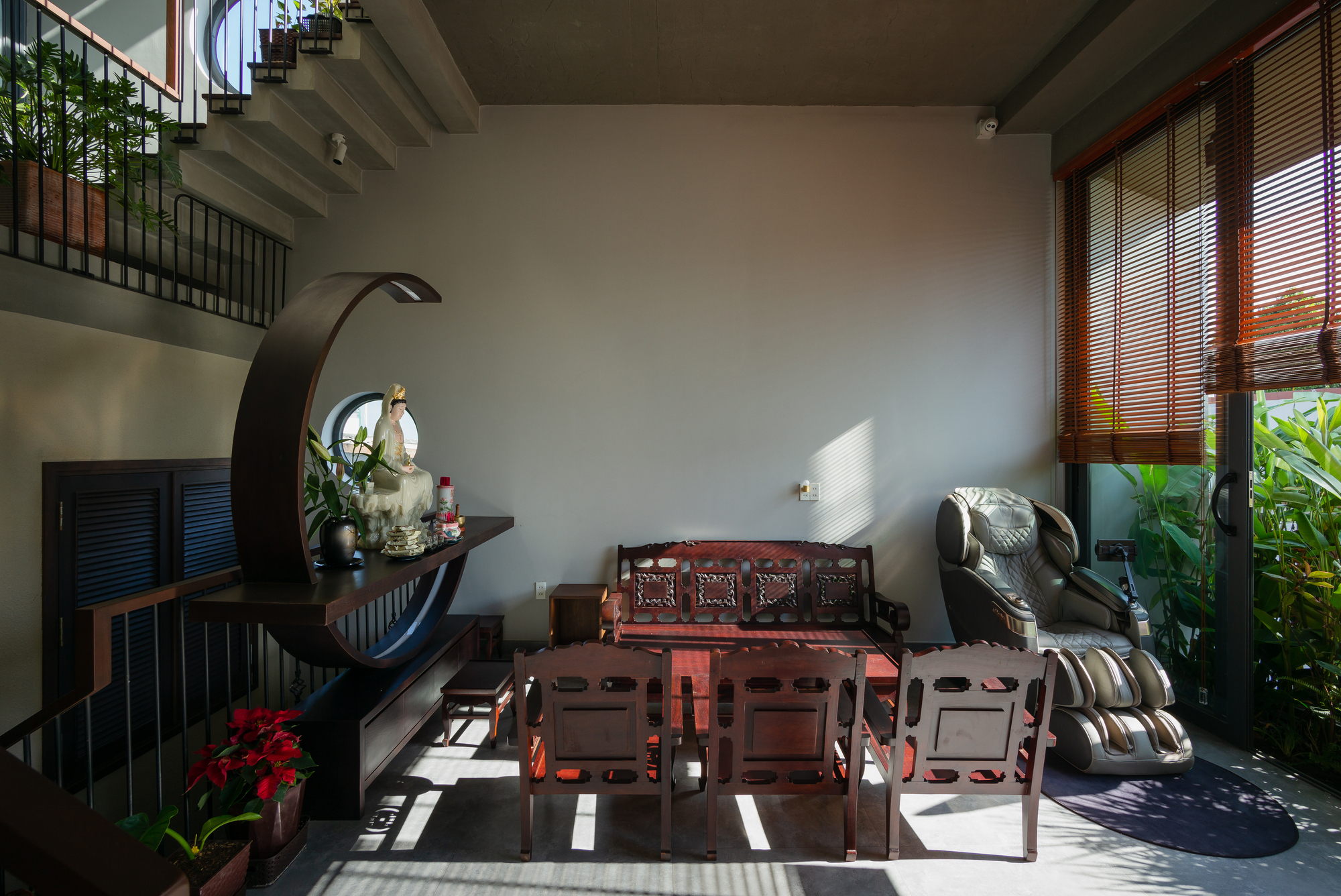 Double-height living room with carved timber furniture and horizontal wood blinds filtering afternoon sunlight