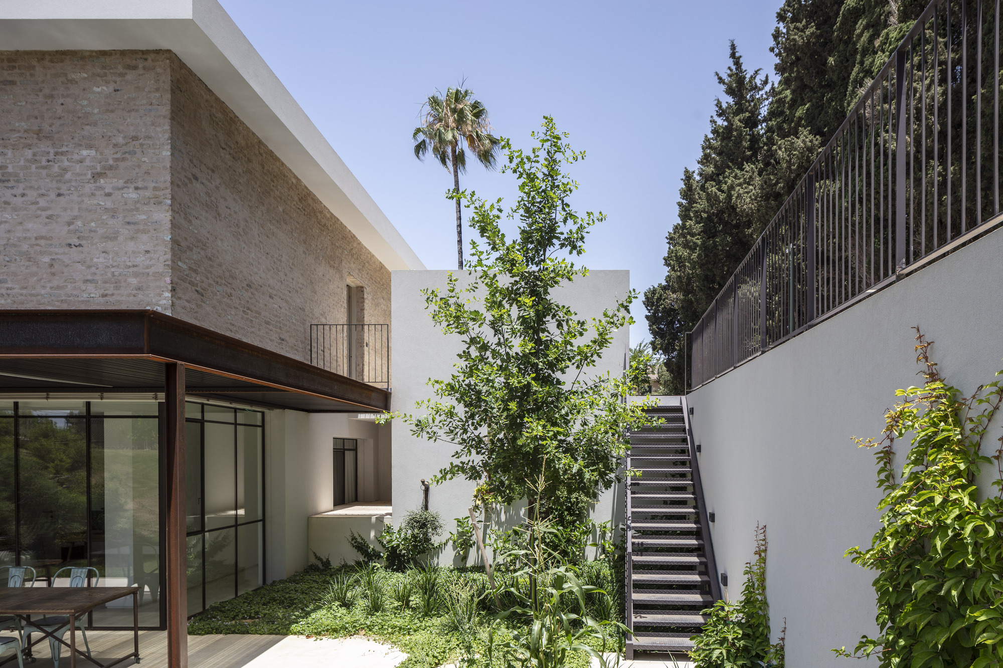 Courtyard with exterior staircase against white wall and planted beds beside the glazed ground floor