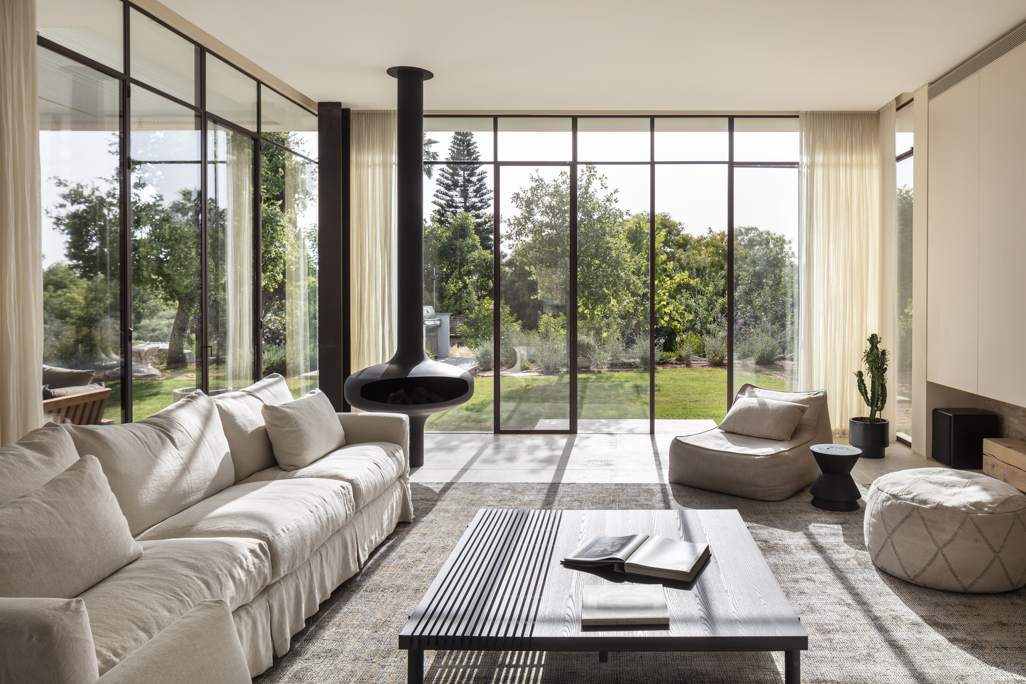 Living room with suspended black fireplace and floor-to-ceiling glazing overlooking the lawn