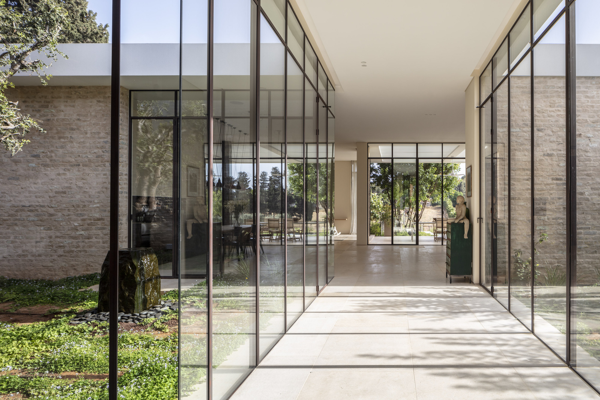 Glass-walled corridor connecting interior spaces with views to planted courtyard on one side