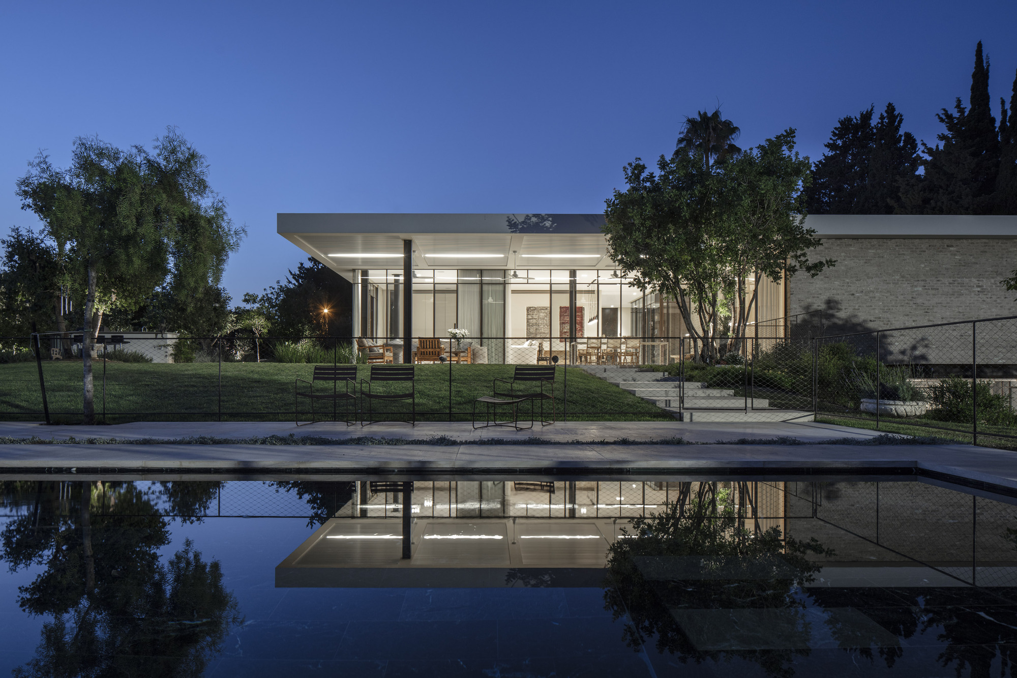 Glass pavilion with flat roof reflected in a still pool at dusk