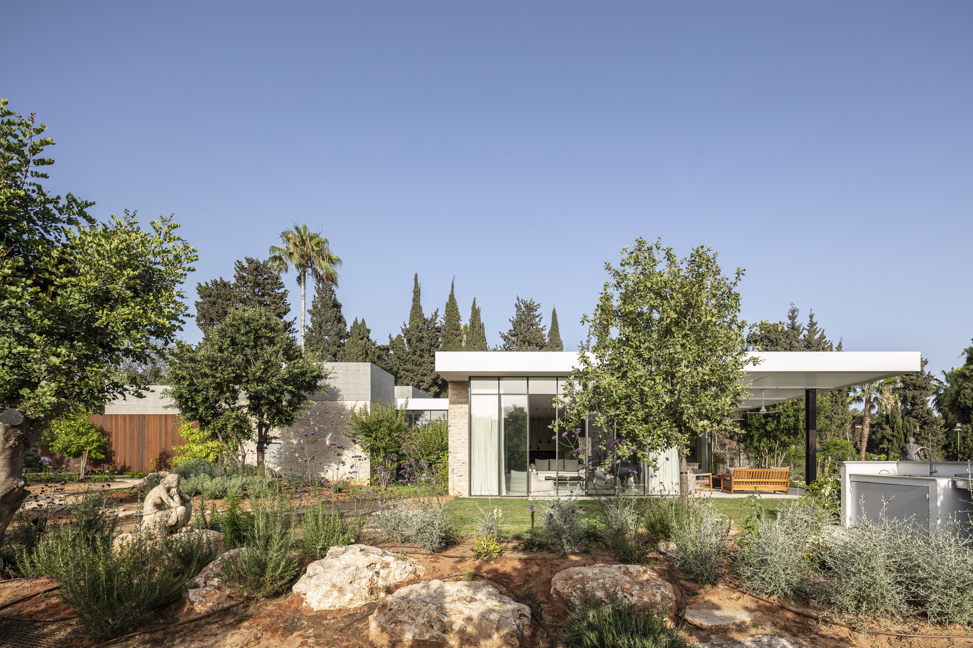 Low-slung pavilions with flat roofs arranged around a planted courtyard with limestone boulders