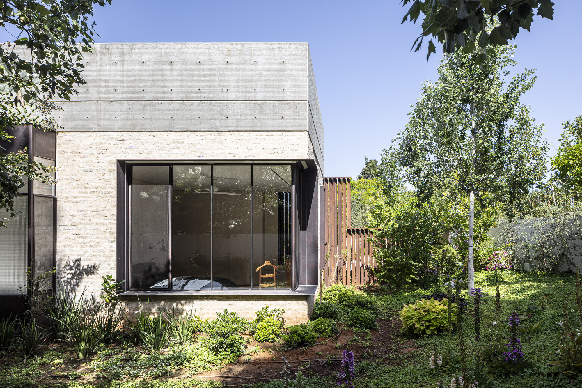 Concrete box with corner window and timber screen wall surrounded by garden beds
