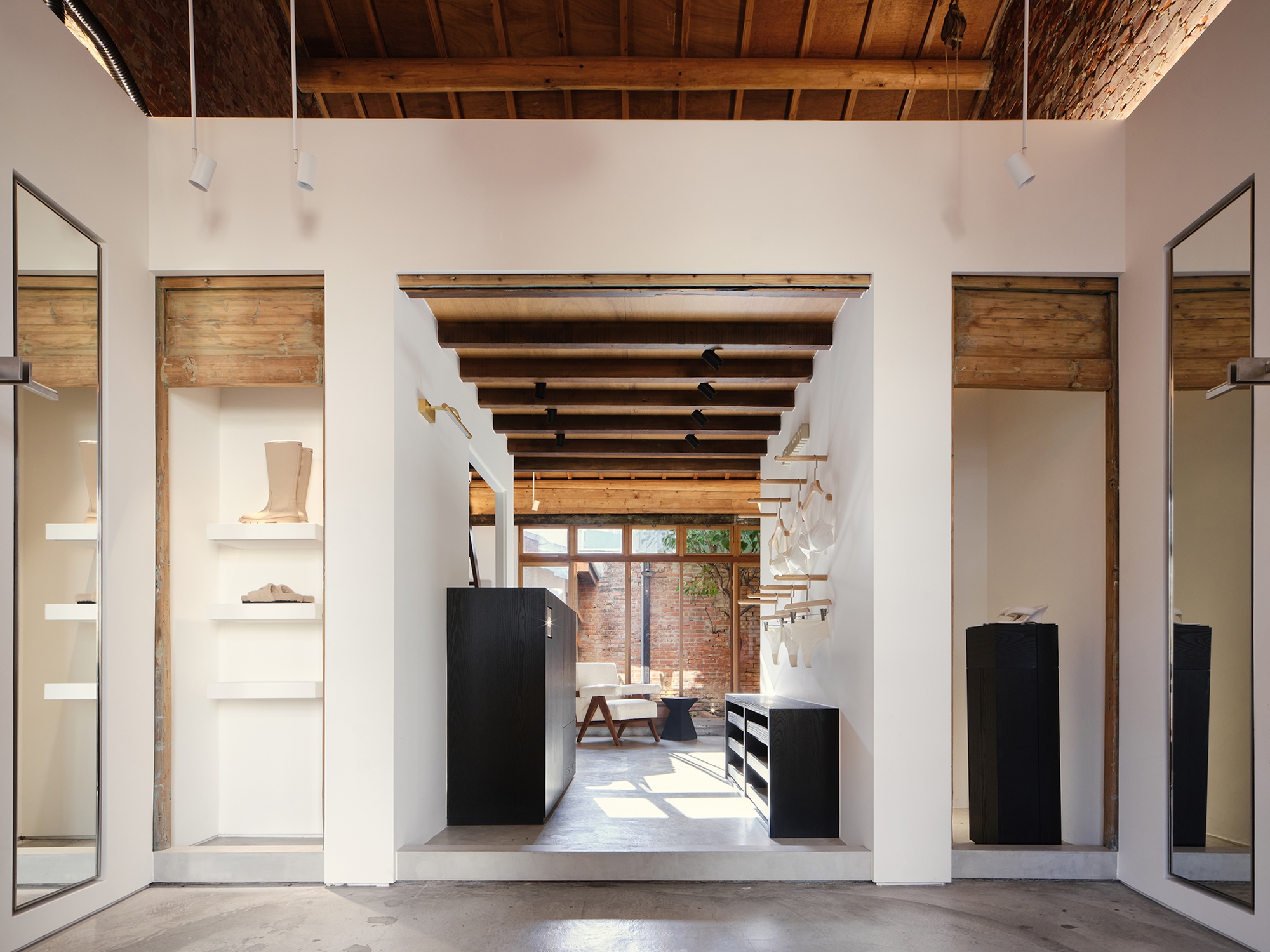 Axial view through white volumes with exposed timber beams and black display units toward a sunlit courtyard