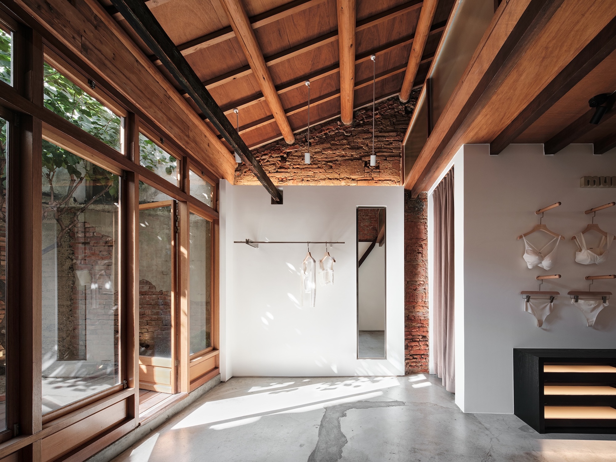 Interior room with timber-framed glazing overlooking courtyard, concrete floor, and dappled afternoon light