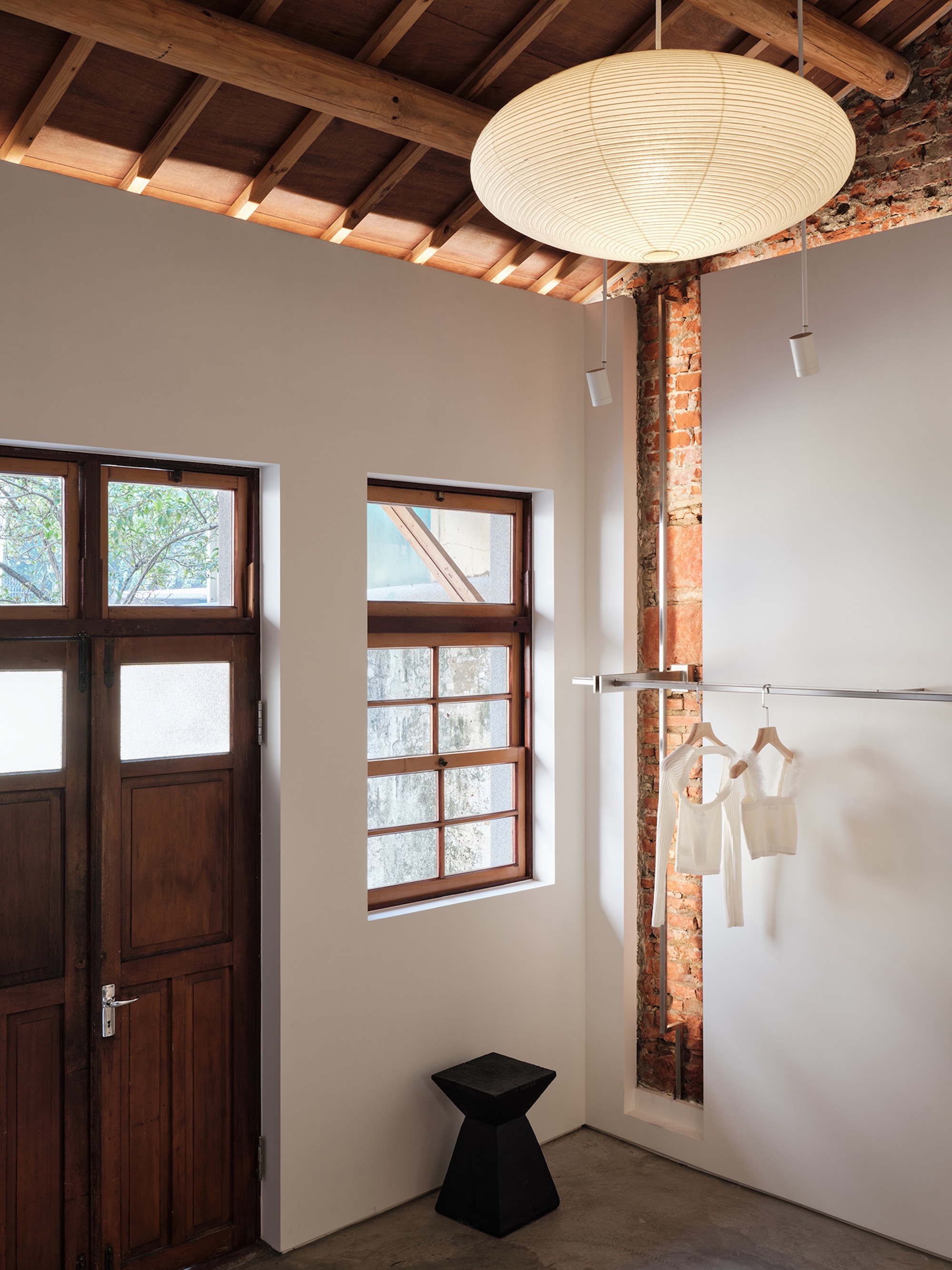 Interior entry space with exposed timber ceiling rafters, white paper lantern and reclaimed brick column