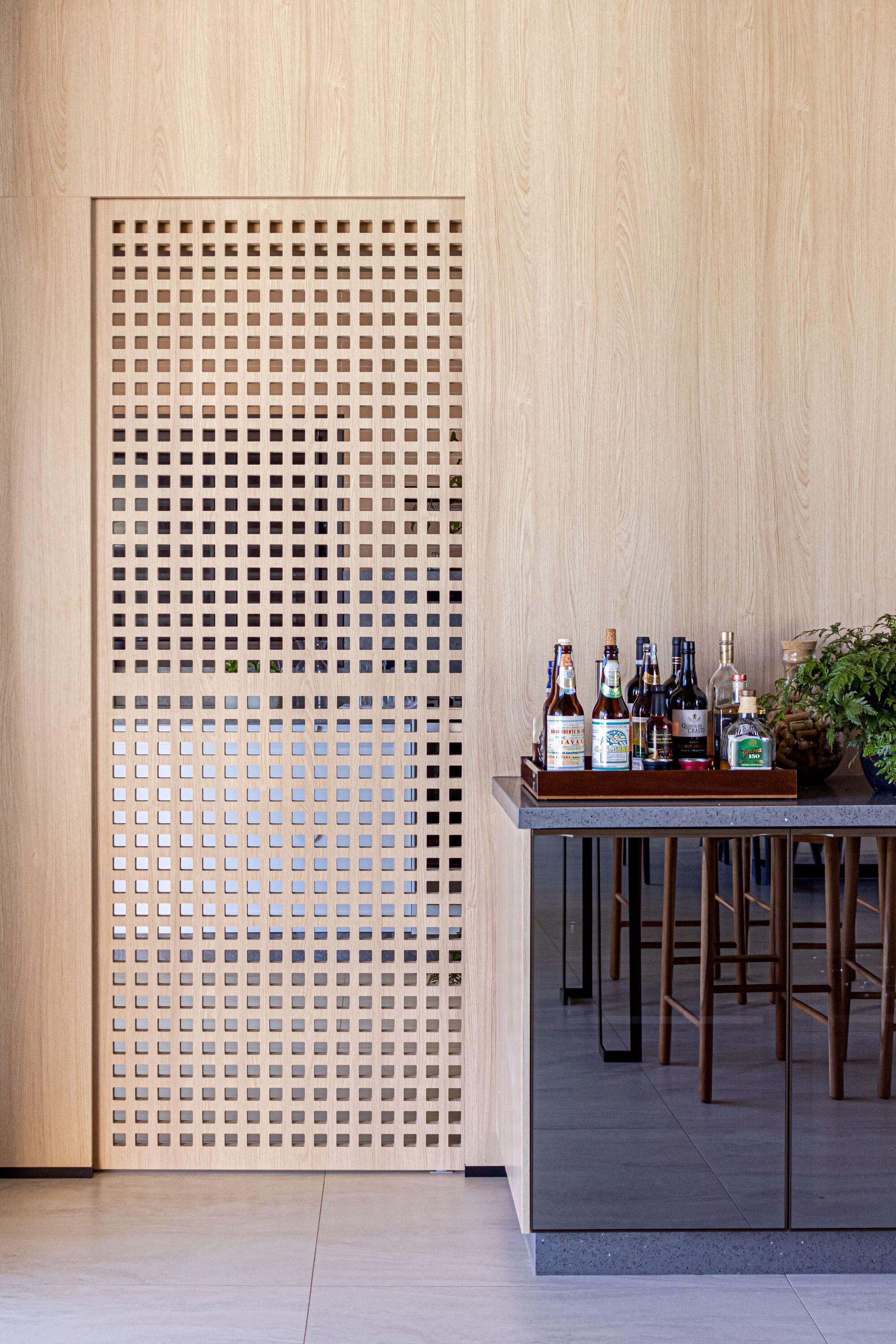Close-up of perforated timber screen panel beside a bar cart with bottles
