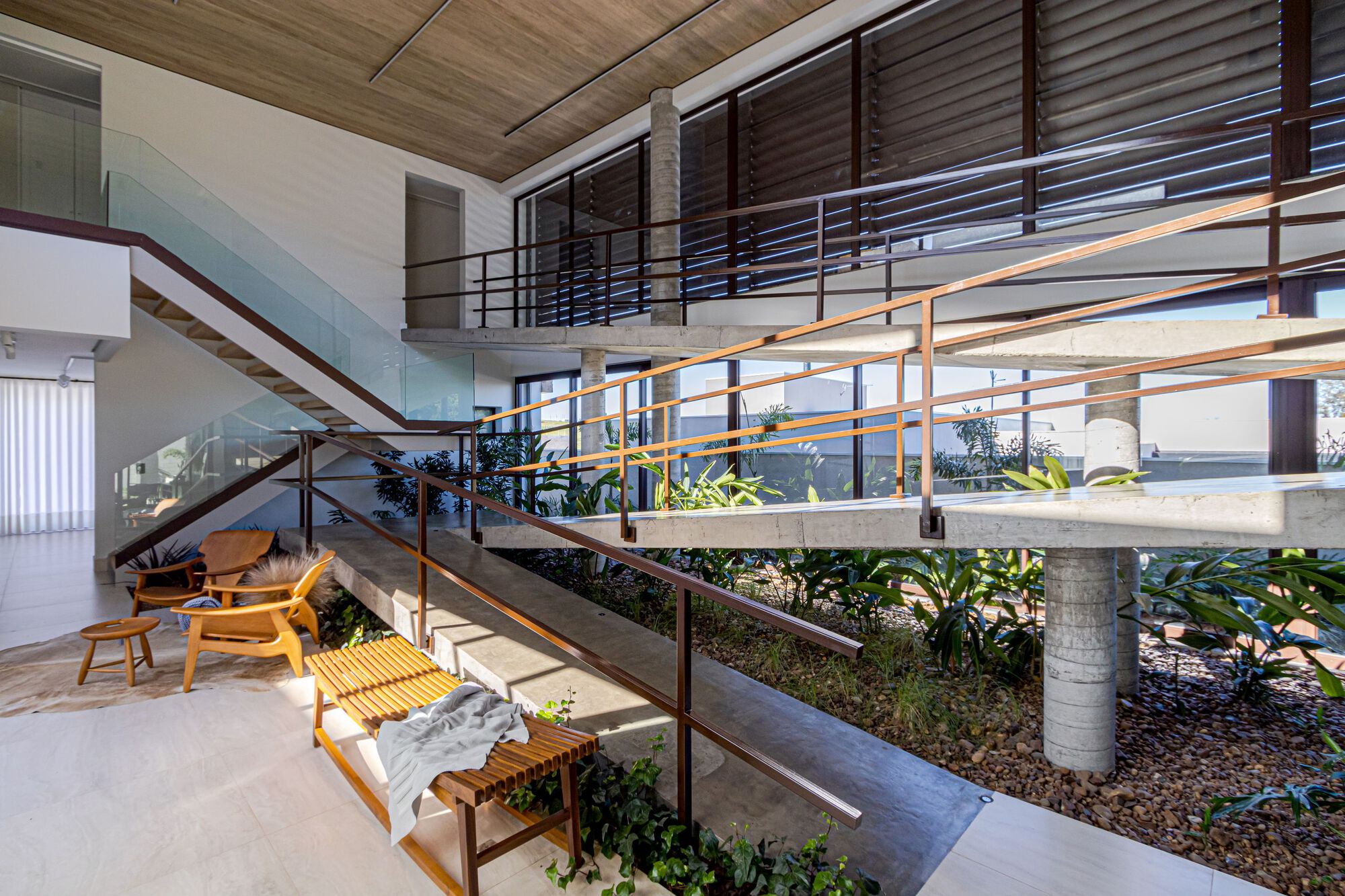 Double-height interior with sunken planted bed, metal railings and timber ceiling under afternoon light