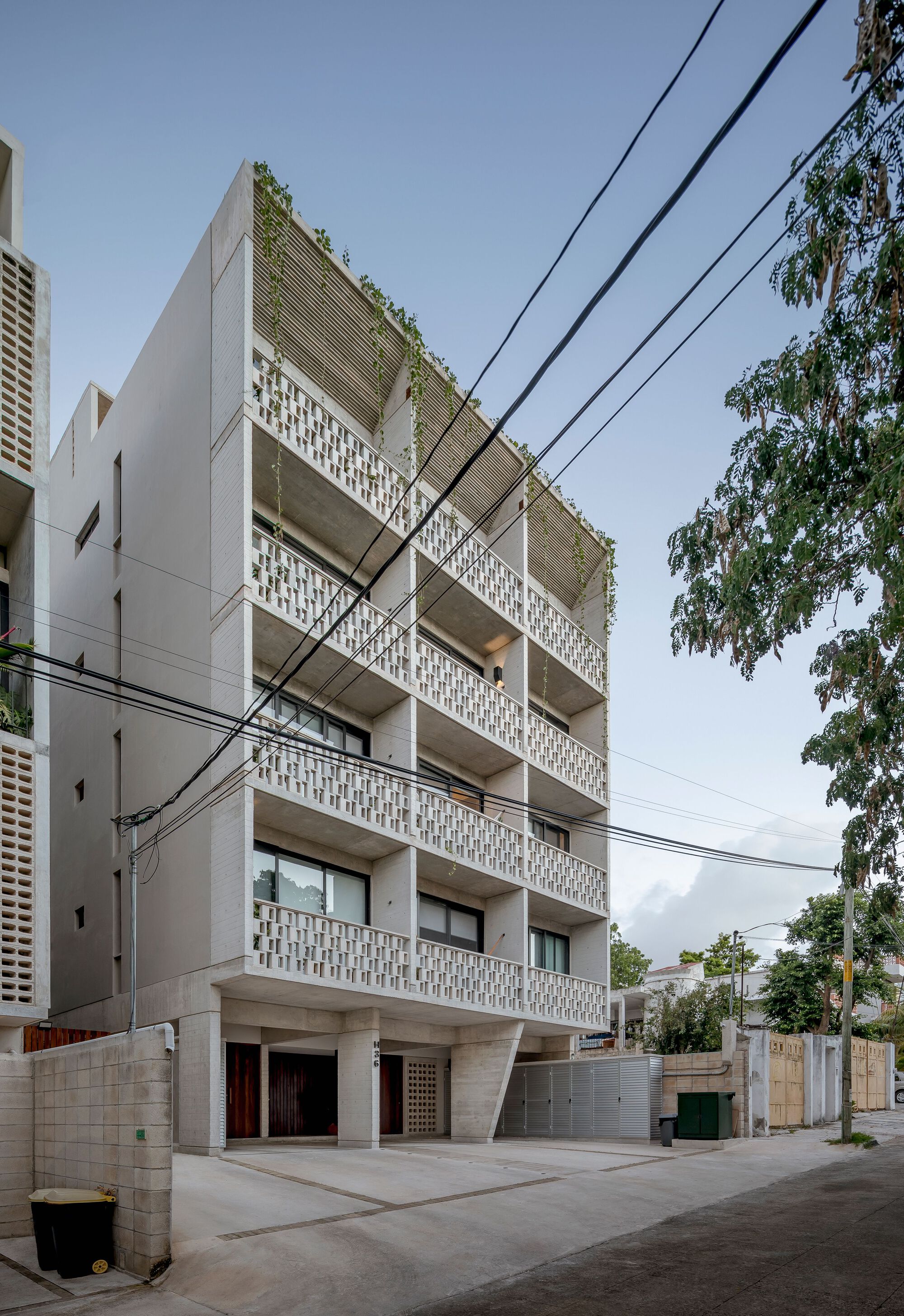 Street view of the five-story facade with perforated concrete screens and rooftop planting beneath power lines
