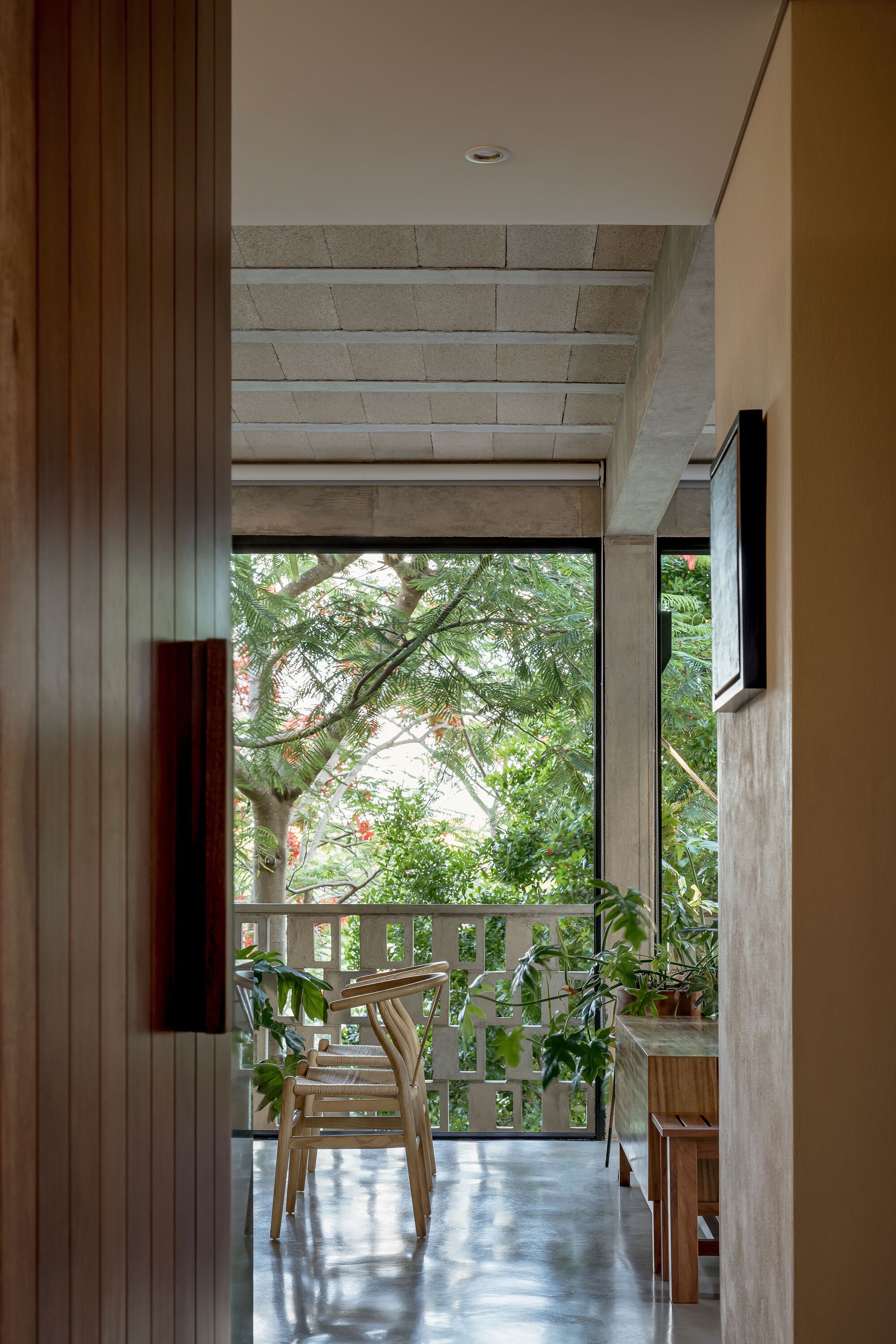 Interior view through doorway to outdoor terrace with wooden chair and tree foliage beyond