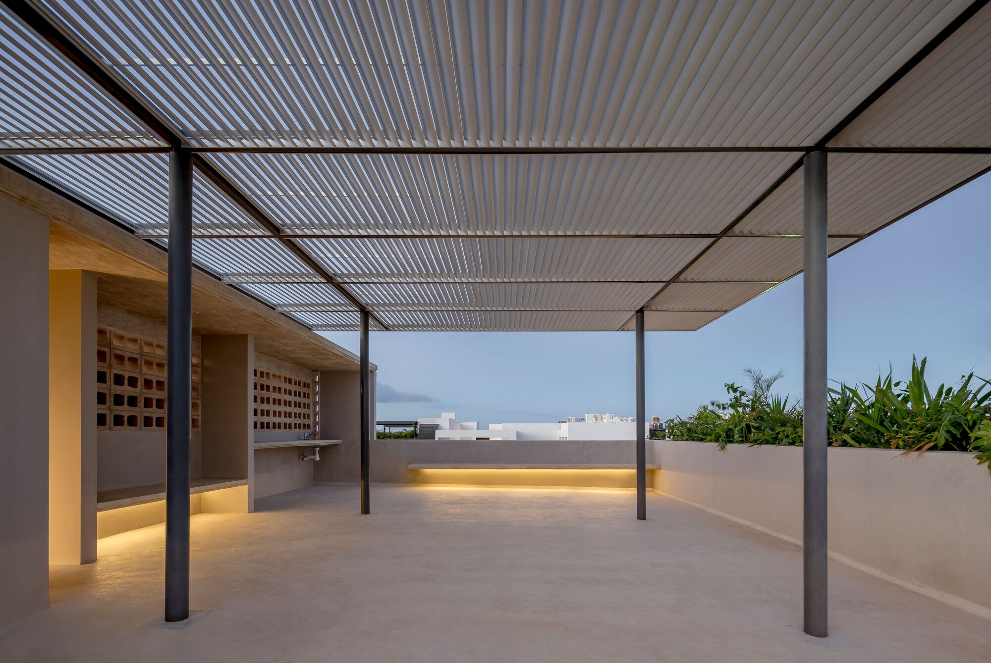 Rooftop terrace with slatted metal canopy on steel columns and integrated planter with tropical foliage at dusk
