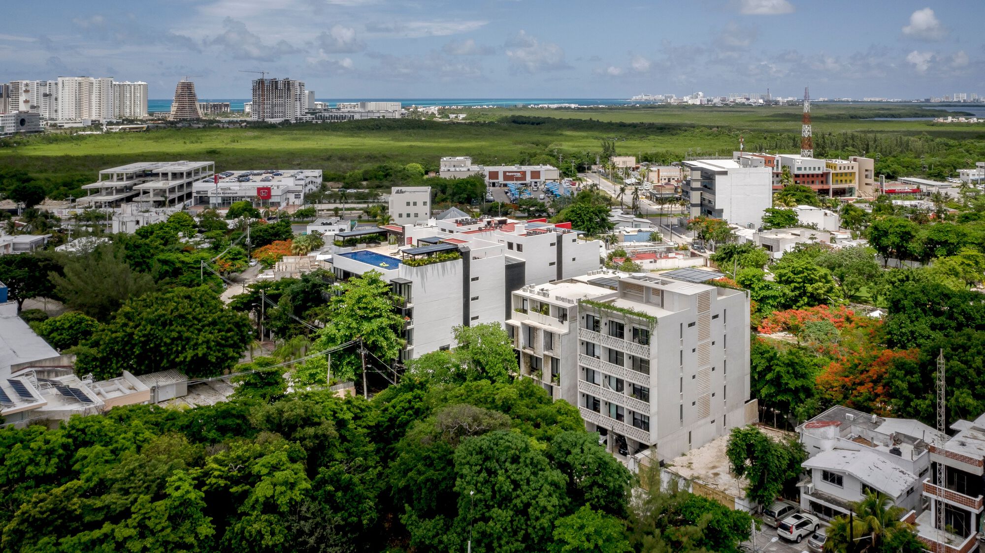 Aerial view of the white residential building surrounded by dense tree canopy and neighboring low-rise structures