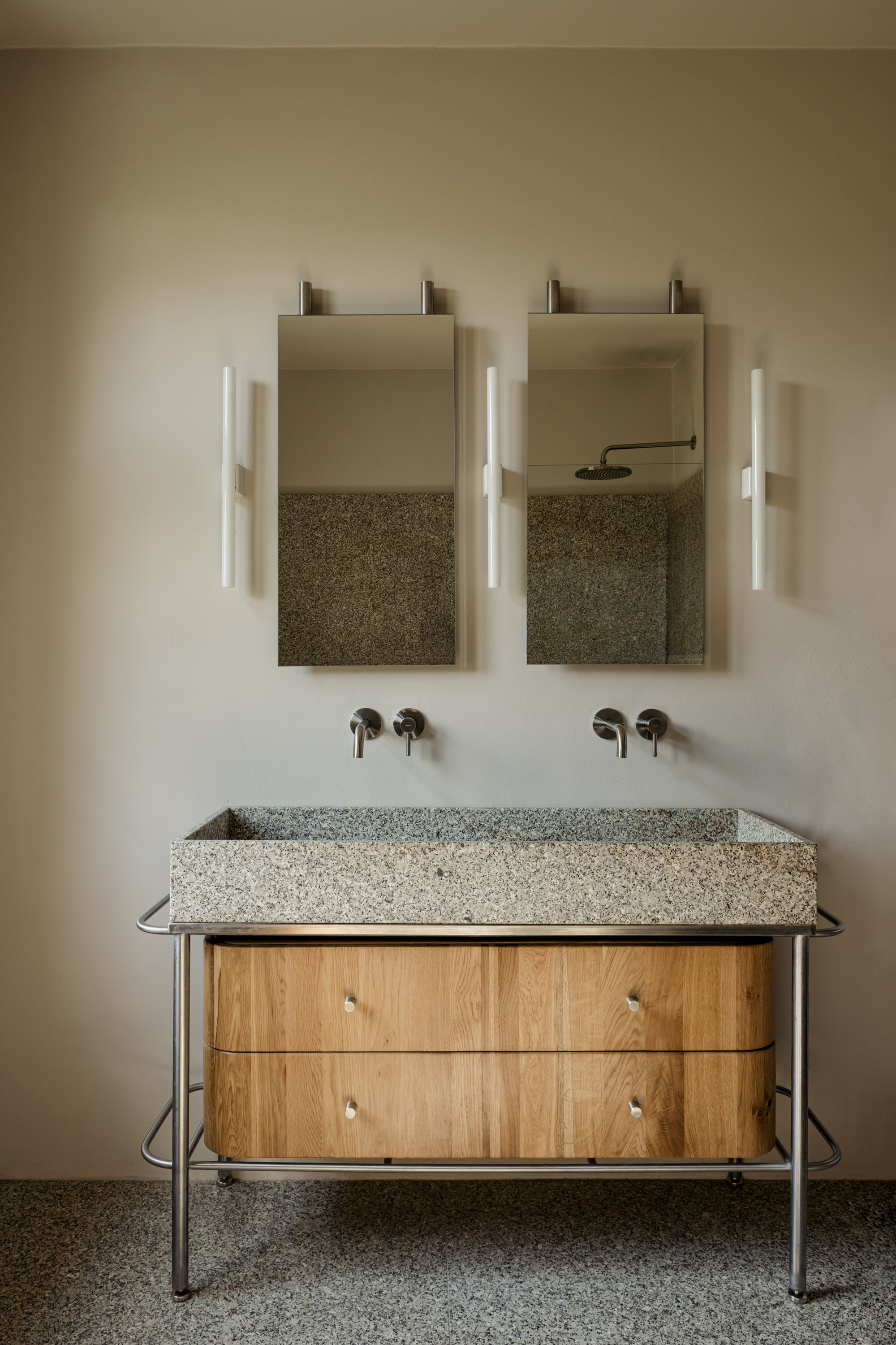 Double vanity with terrazzo sink on tubular steel frame below wall-mounted mirrors and sconces