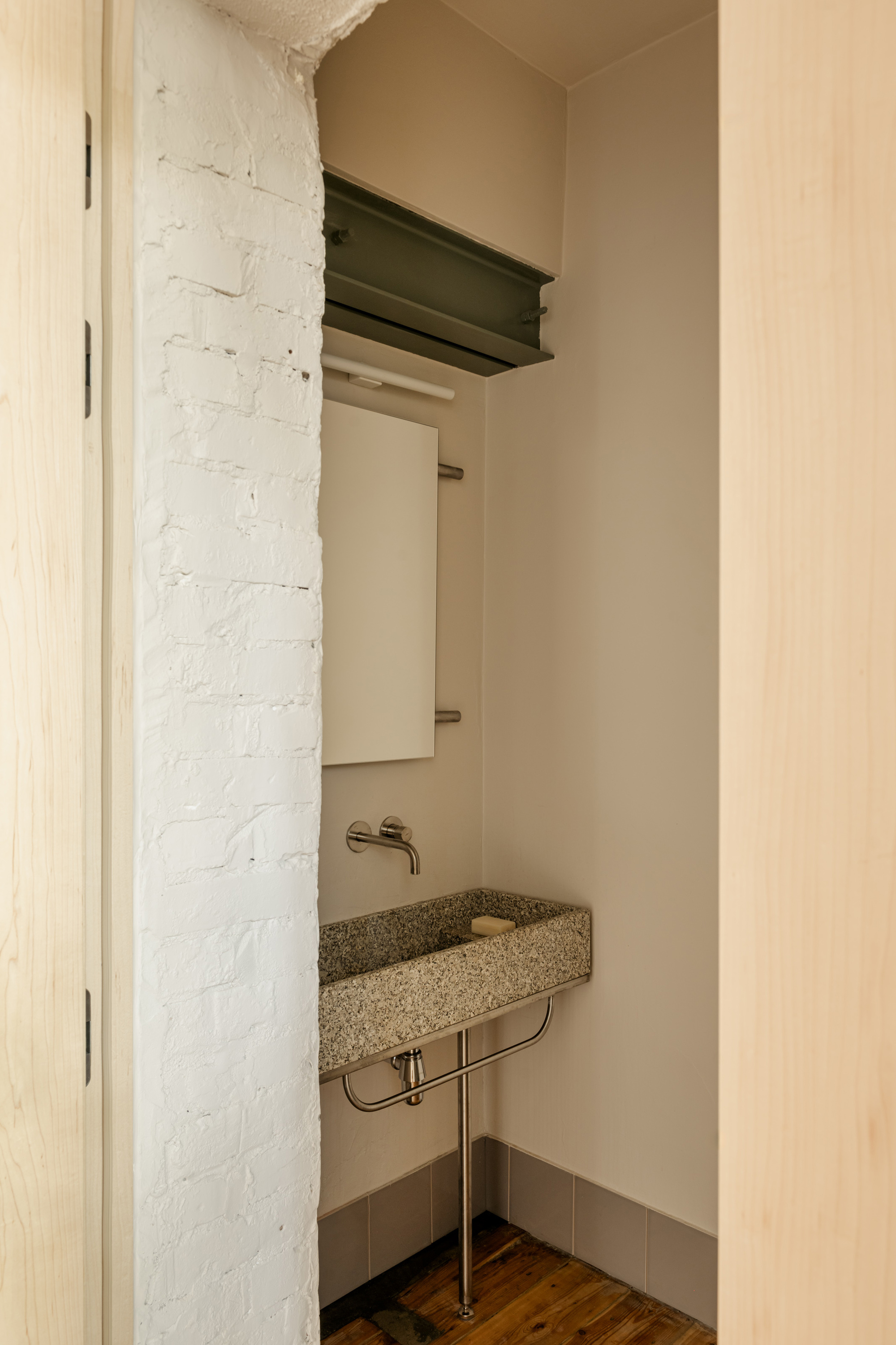 Compact powder room with terrazzo basin on metal stand beside painted brick wall