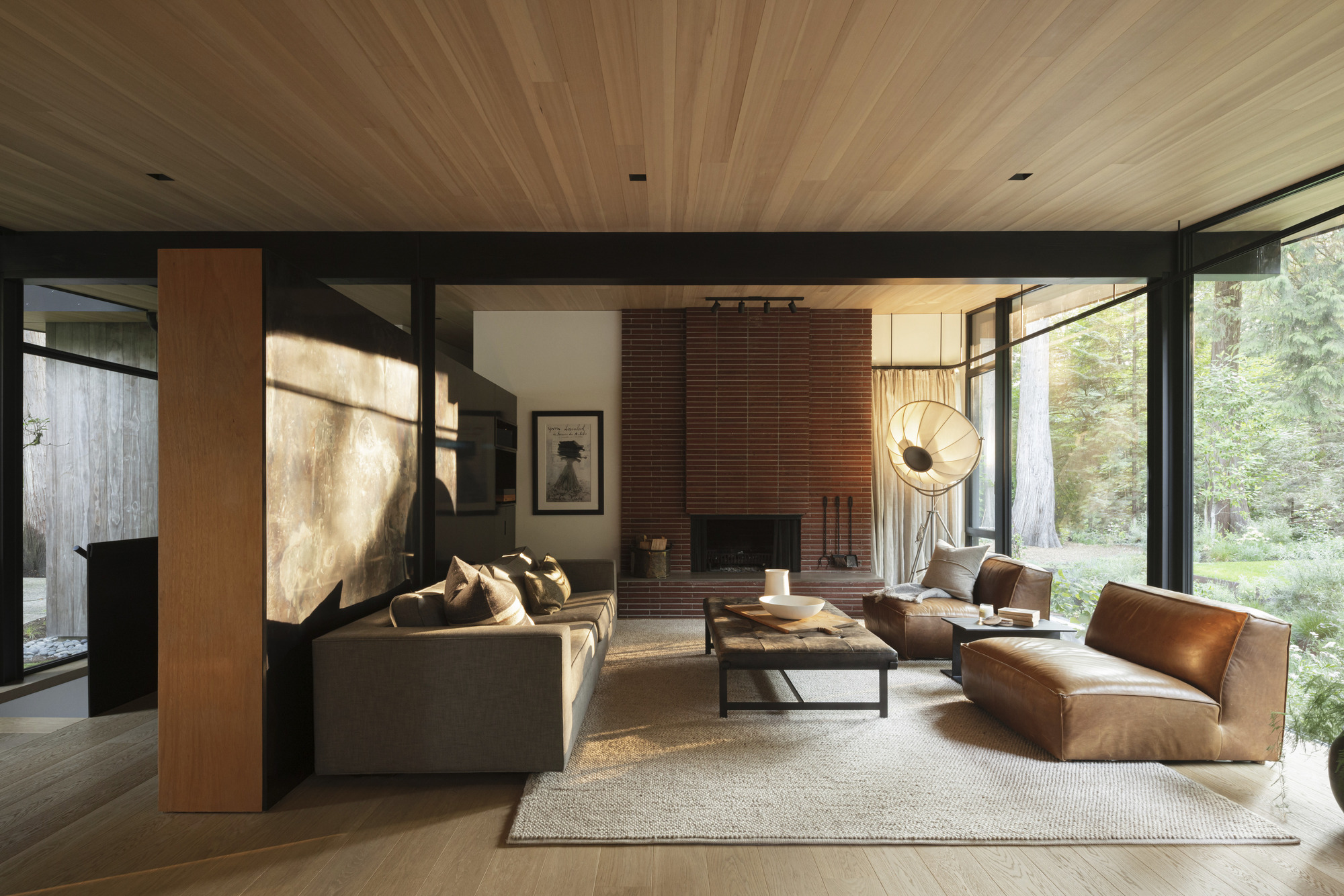 Living room with ribbed wood ceiling, red brick fireplace, and full-height glazing to garden