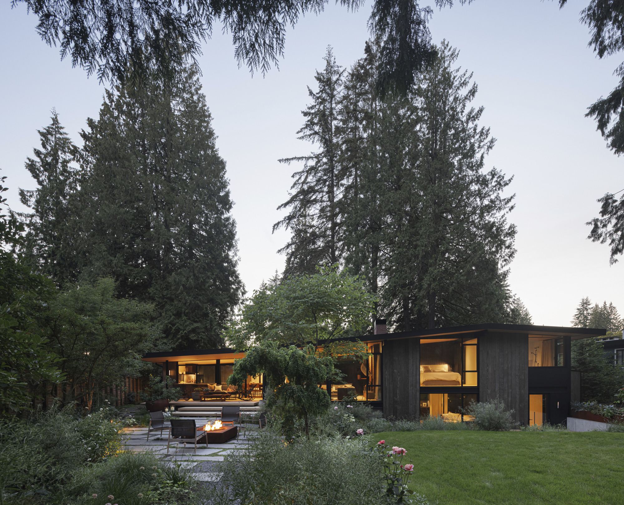 Garden view showing pavilions connected by low roof planes among mature conifers at twilight