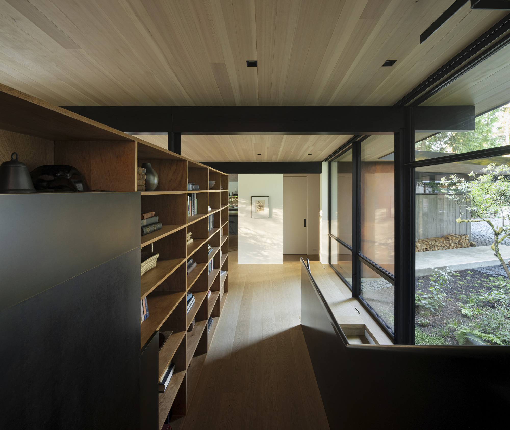 Timber shelving corridor with black steel beams and glazed wall opening to a courtyard