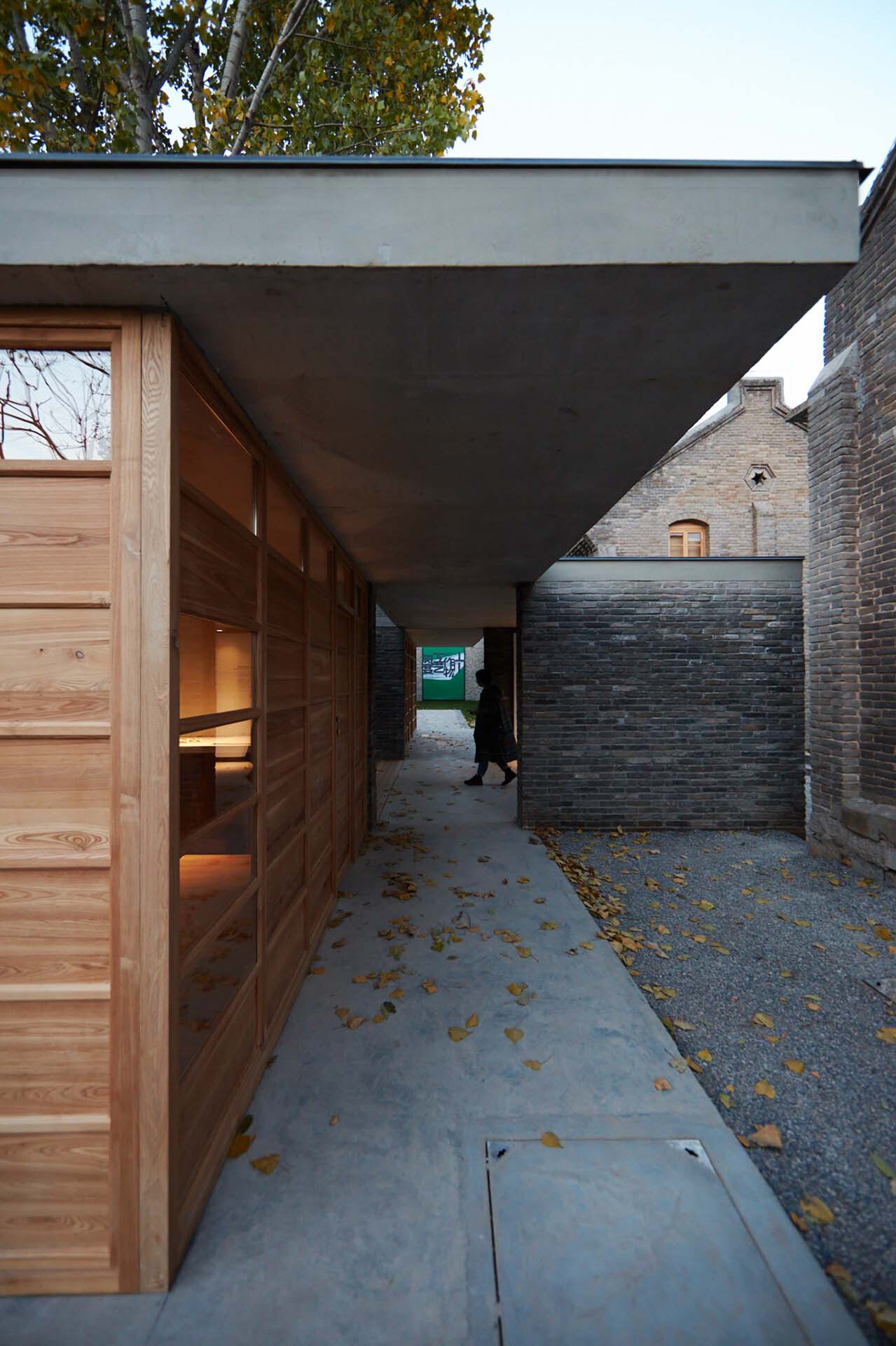 Covered entry passage with timber sliding doors and concrete soffit between brick walls scattered with autumn leaves