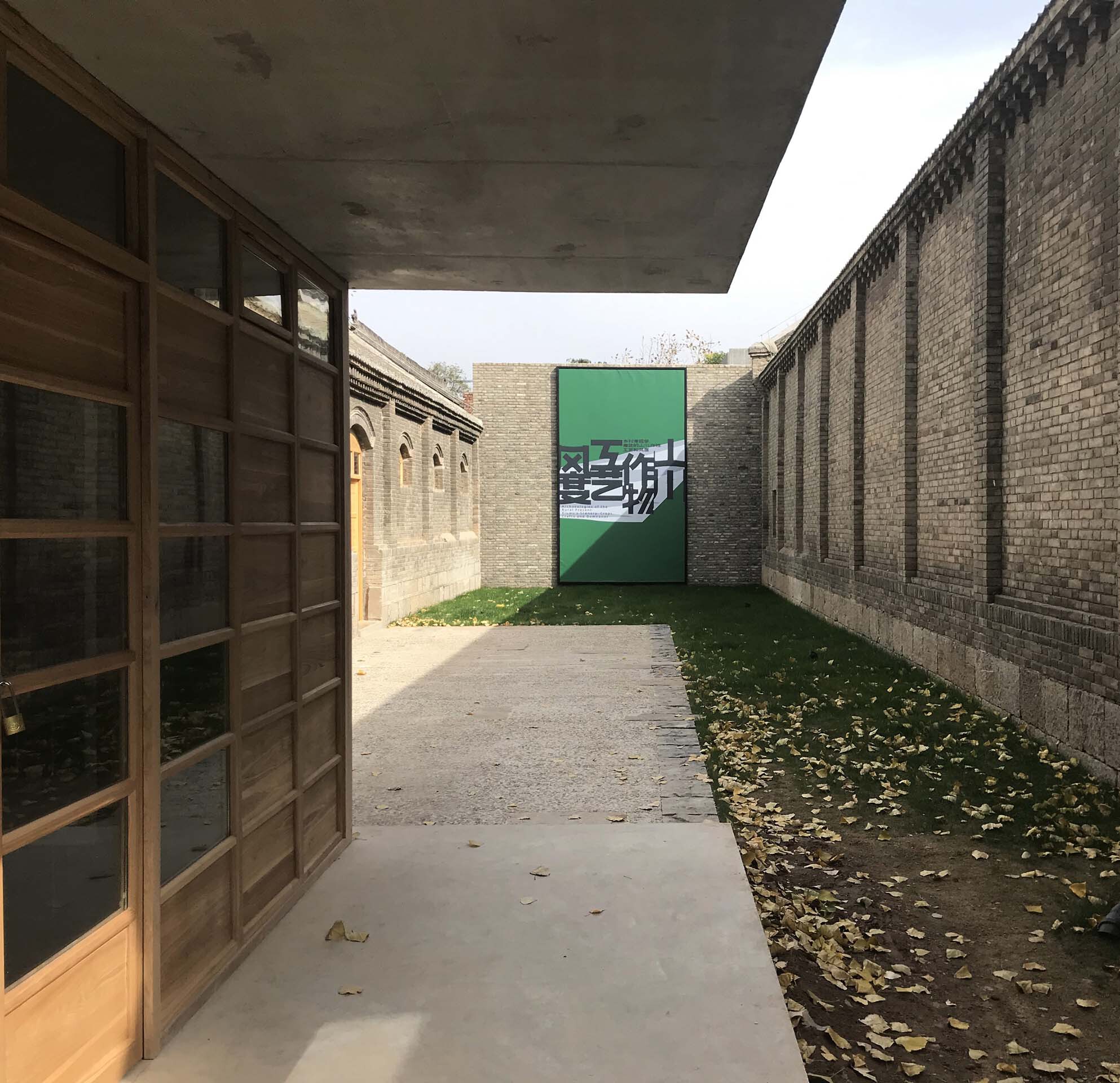 Concrete canopy sheltering a passage with timber screen and green painted door with graphic at the end