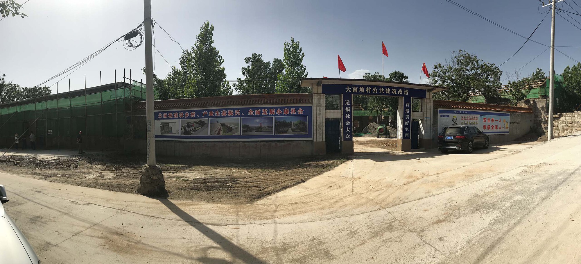 Wide-angle street view showing compound entrance with green fence and red flags under a cloudy sky