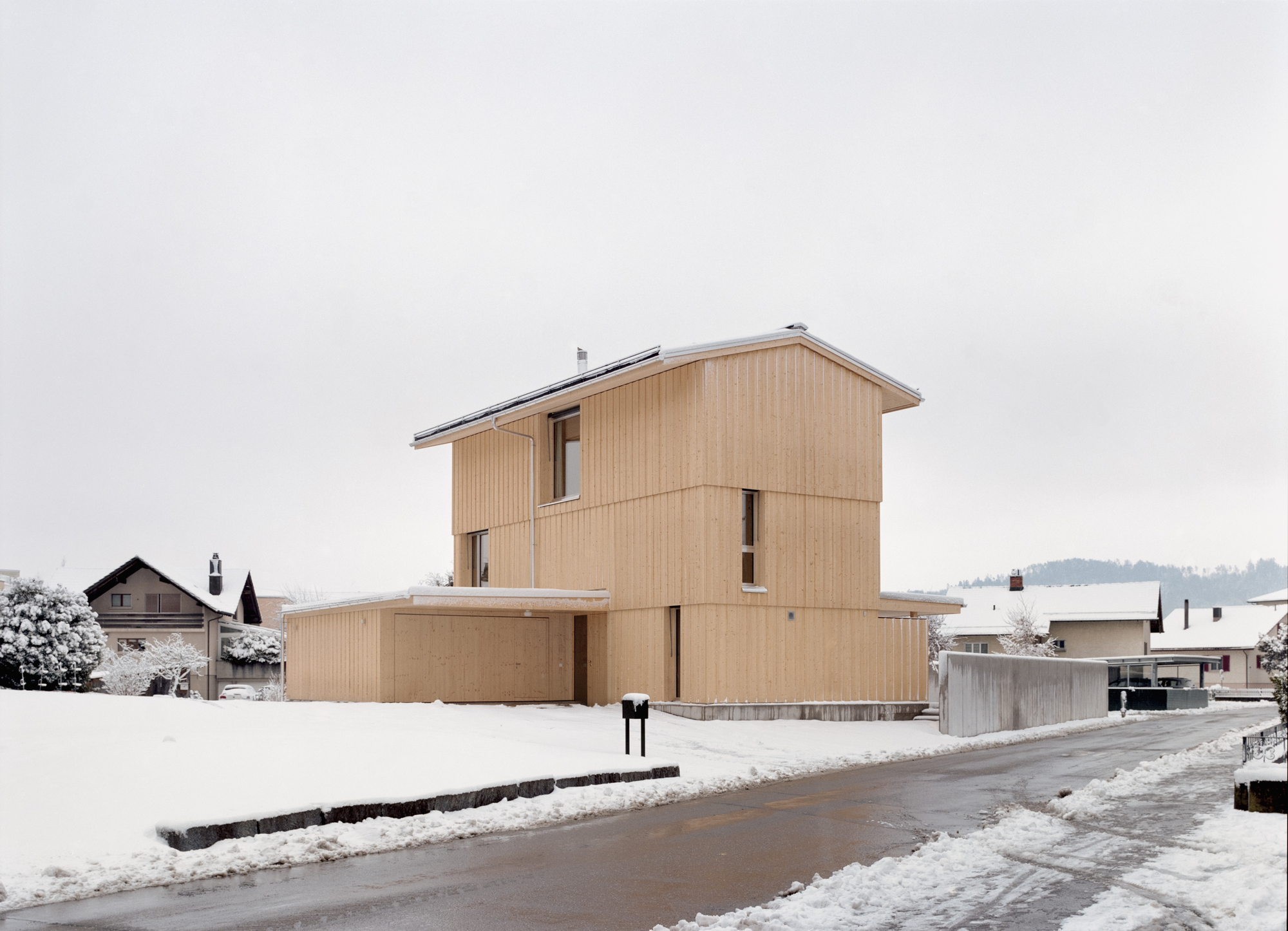 Street facade showing the stacked timber-clad volumes with glazed openings under an overcast winter sky