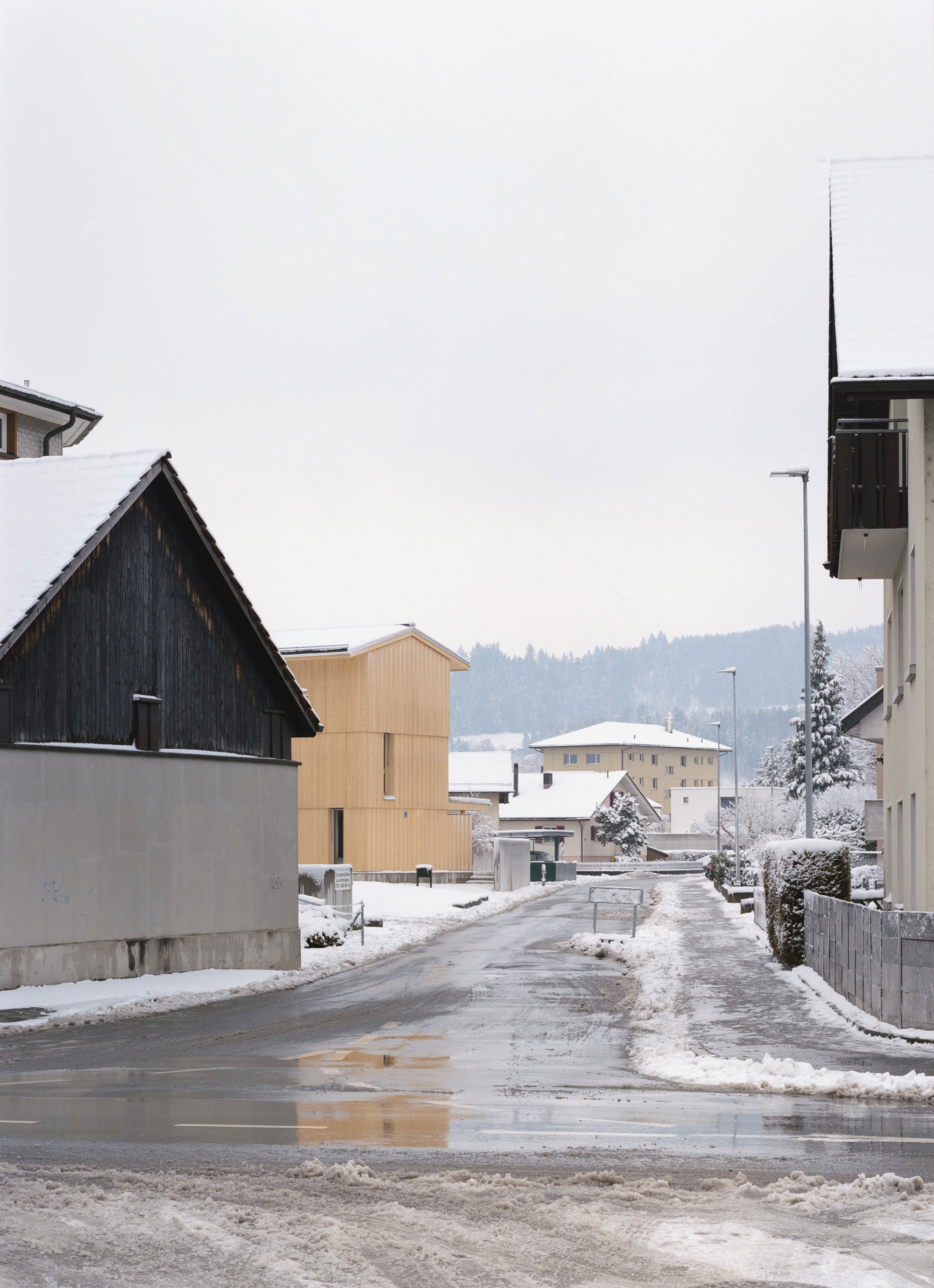 Timber house seen from a residential street intersection in winter with surrounding traditional buildings and forested hills