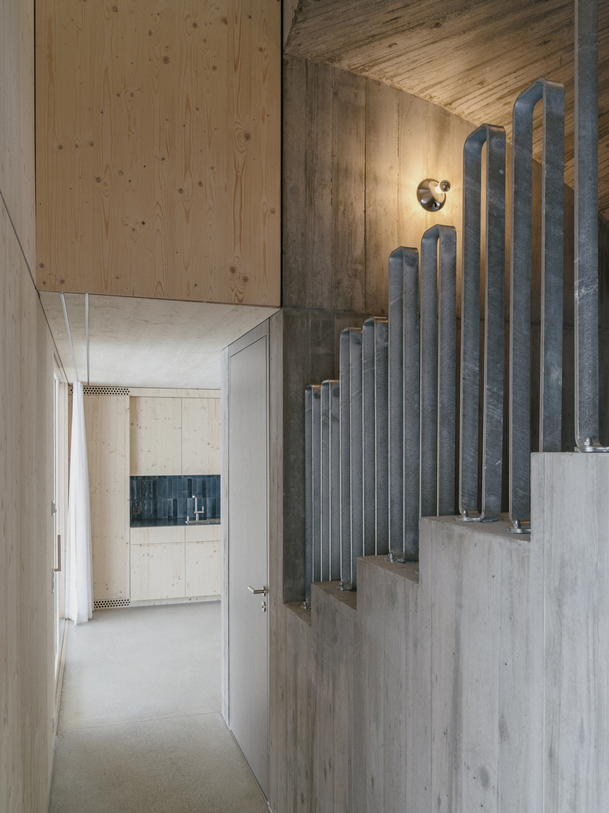 Concrete staircase with vertical metal pipe balustrade ascending through a double-height corridor