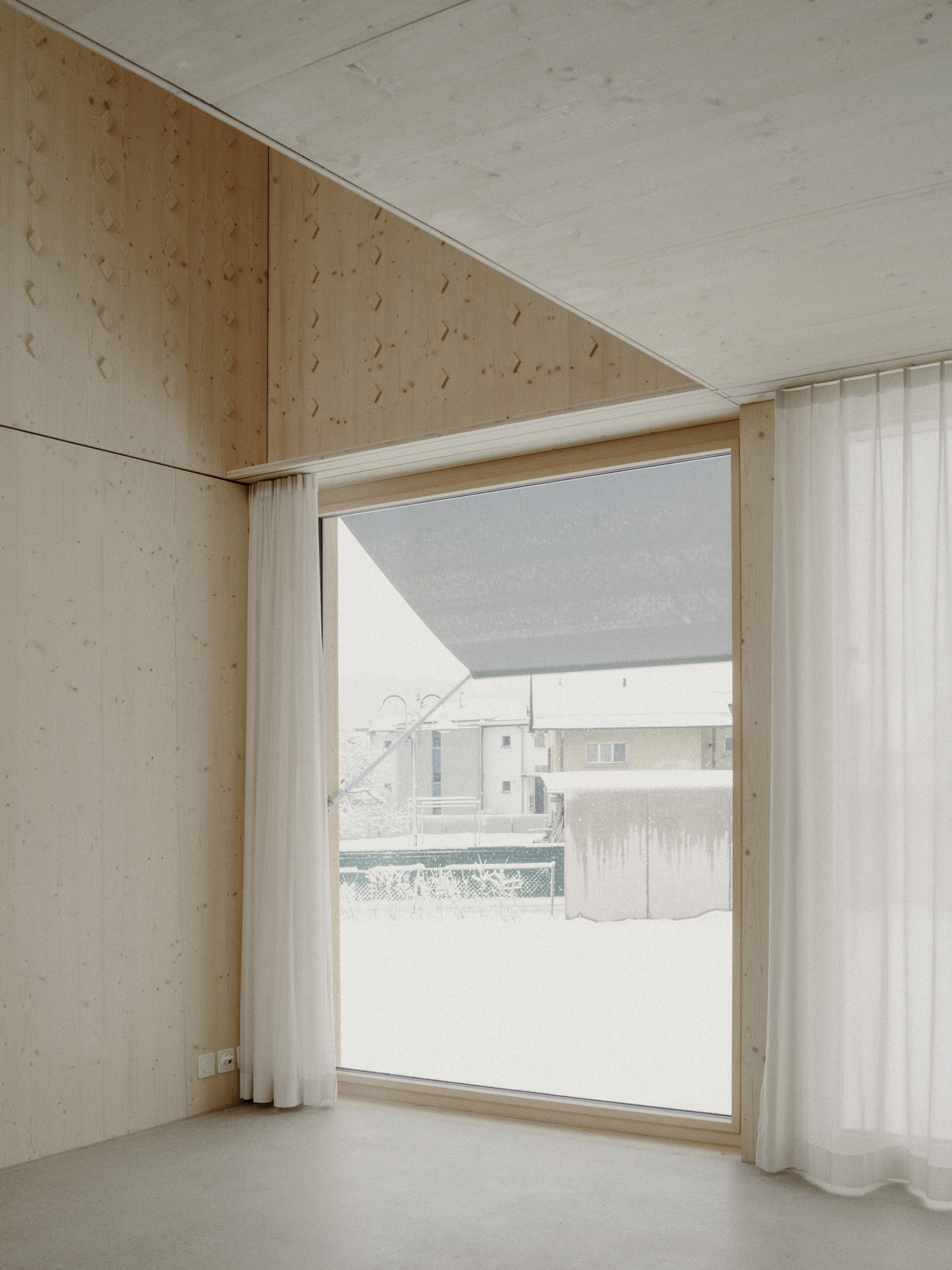 Light plywood interior corner with floor-to-ceiling window framing a snowy courtyard view