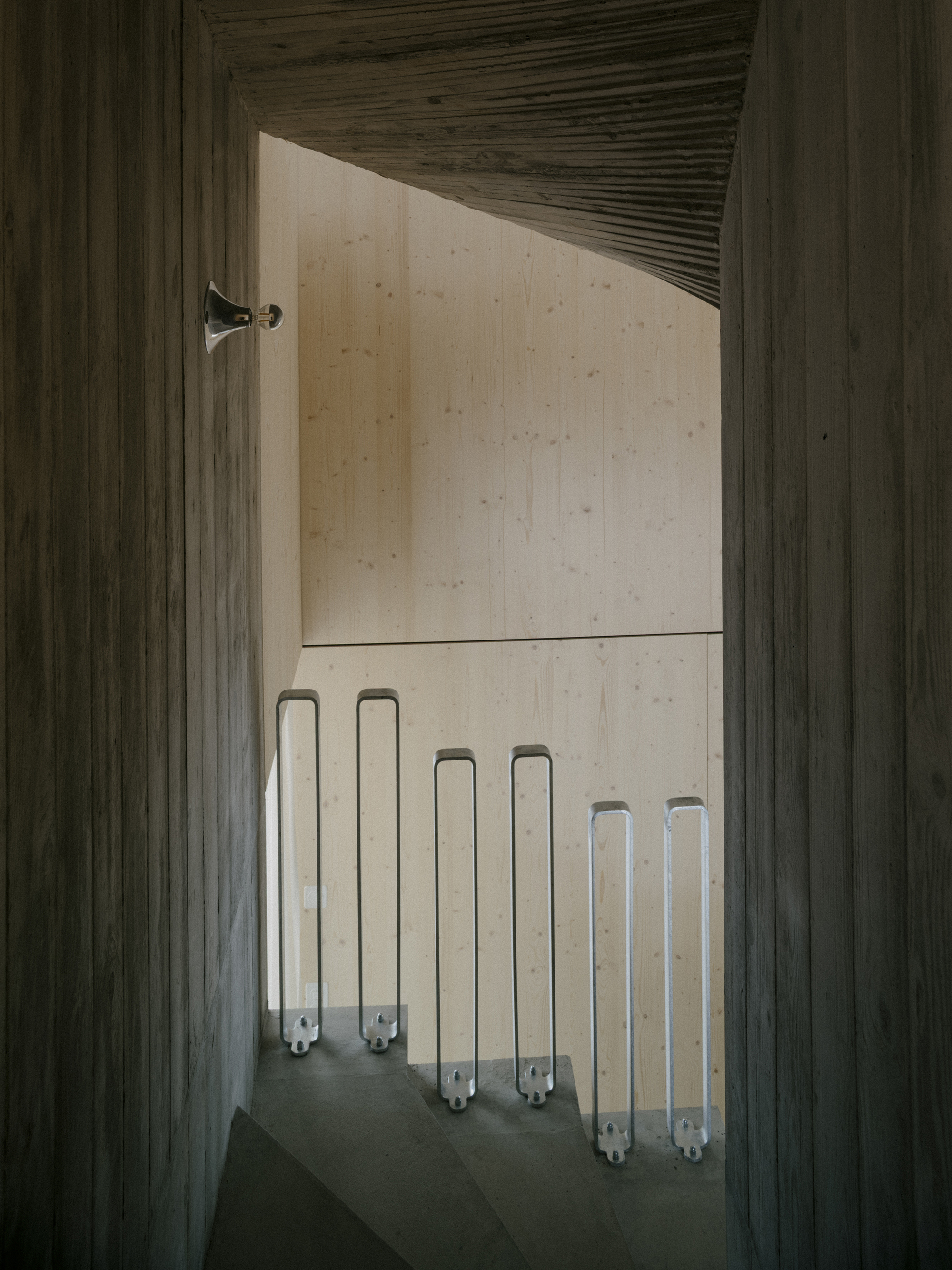 Timber-framed doorway revealing concrete staircase with rows of translucent tube lights along the wall